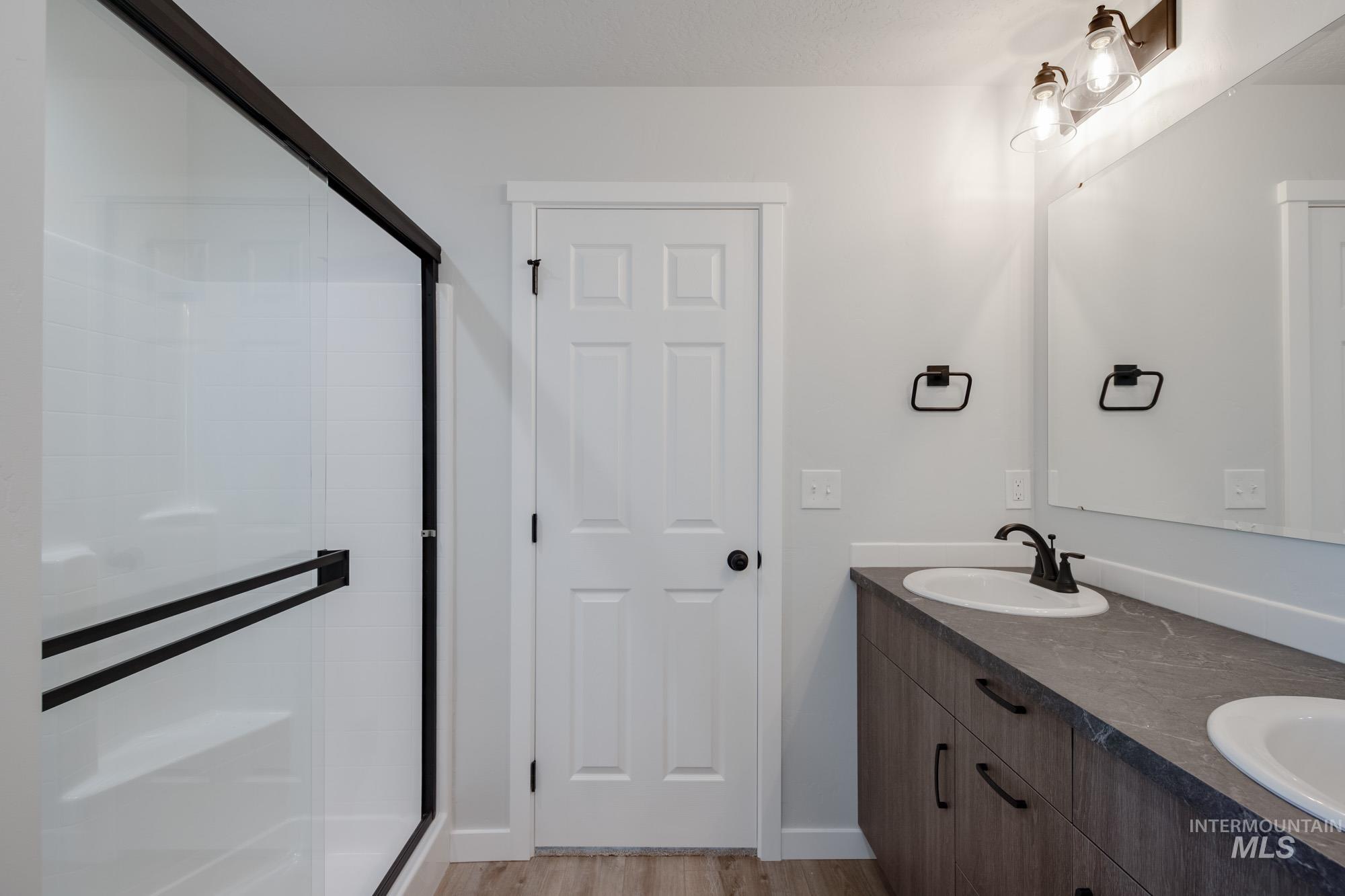 Bathroom with a shower stall, double vanity, and light wood-style floors