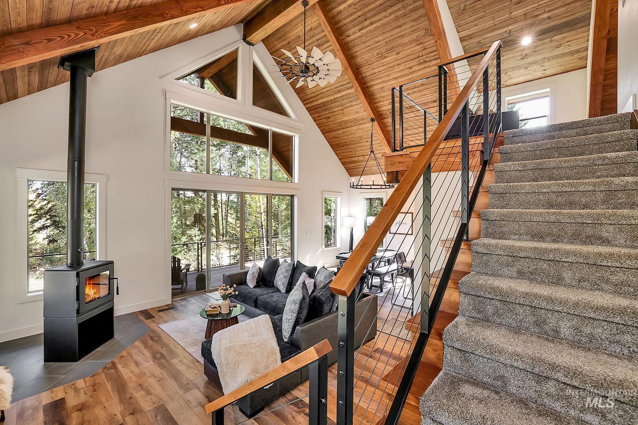 Living room featuring high vaulted ceiling, dark wood-style floors, a wood stove, stairway, and a wood ceiling with exposed beams