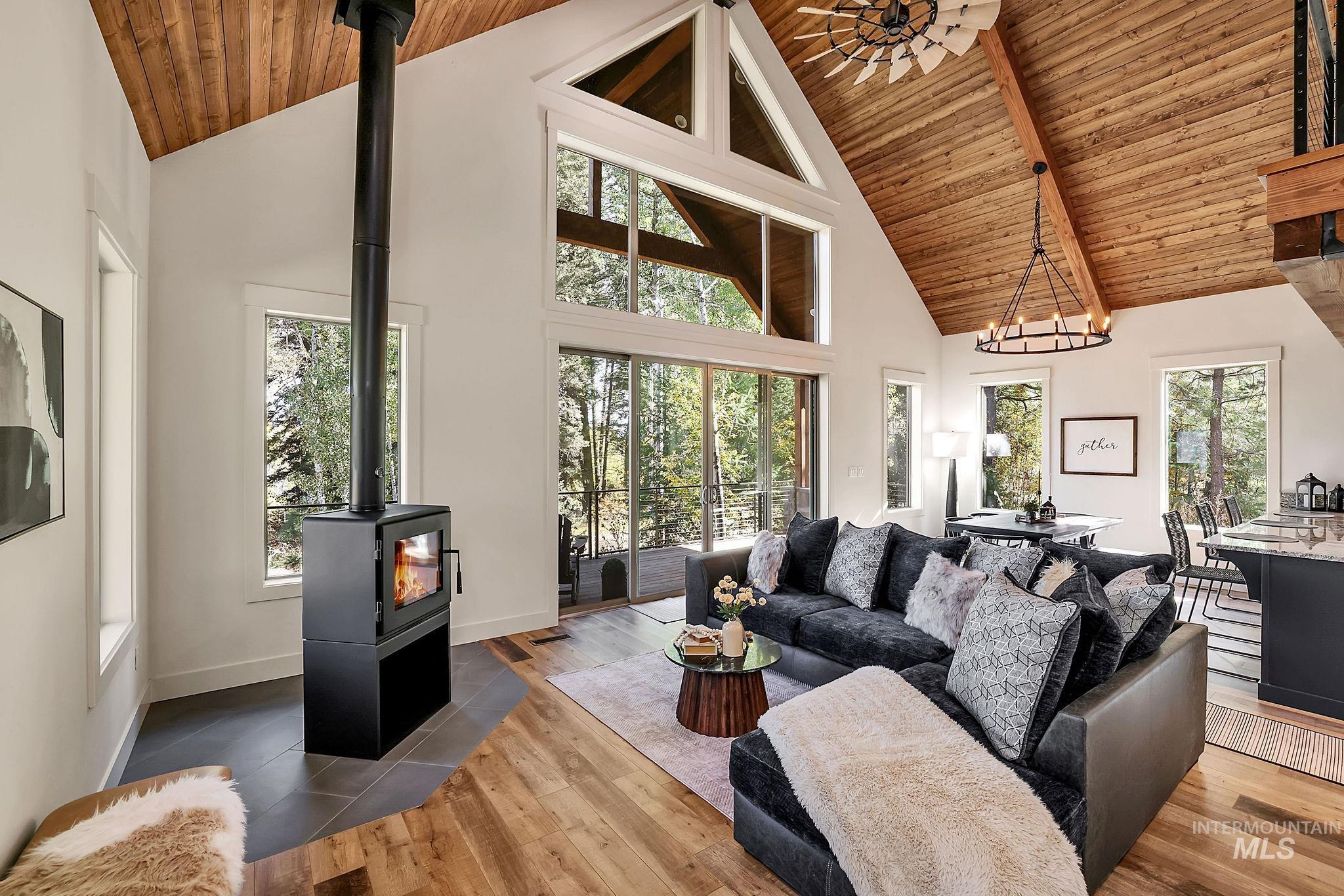 Living area with high vaulted ceiling, hardwood / wood-style floors, wood ceiling, a wood stove, and a chandelier