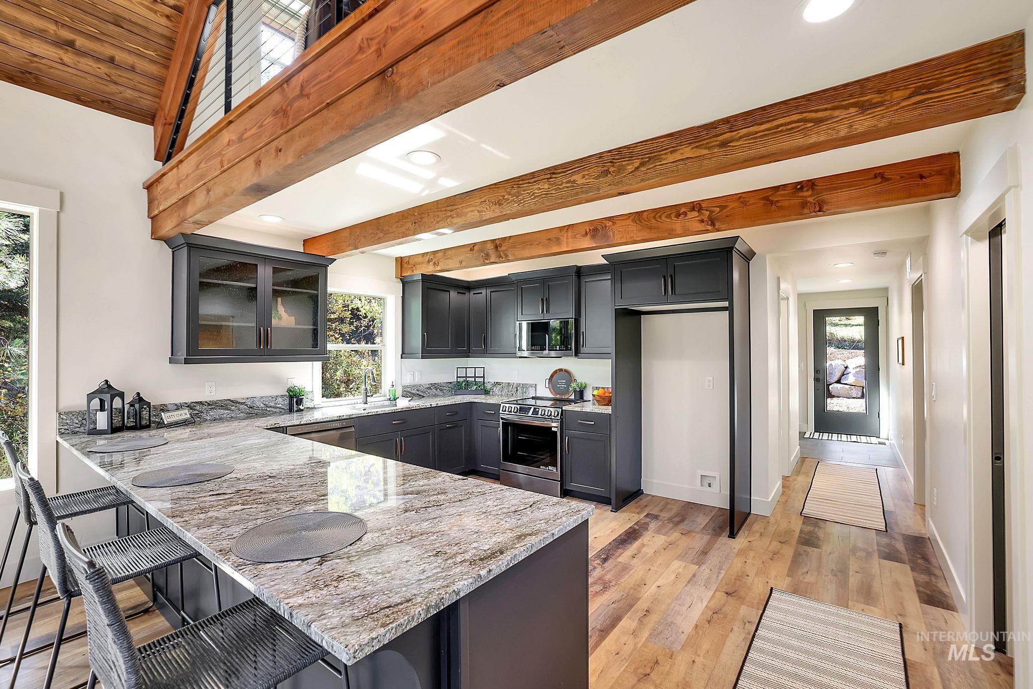 Kitchen featuring beamed ceiling, a kitchen bar, light wood-style floors, light stone counters, and a peninsula