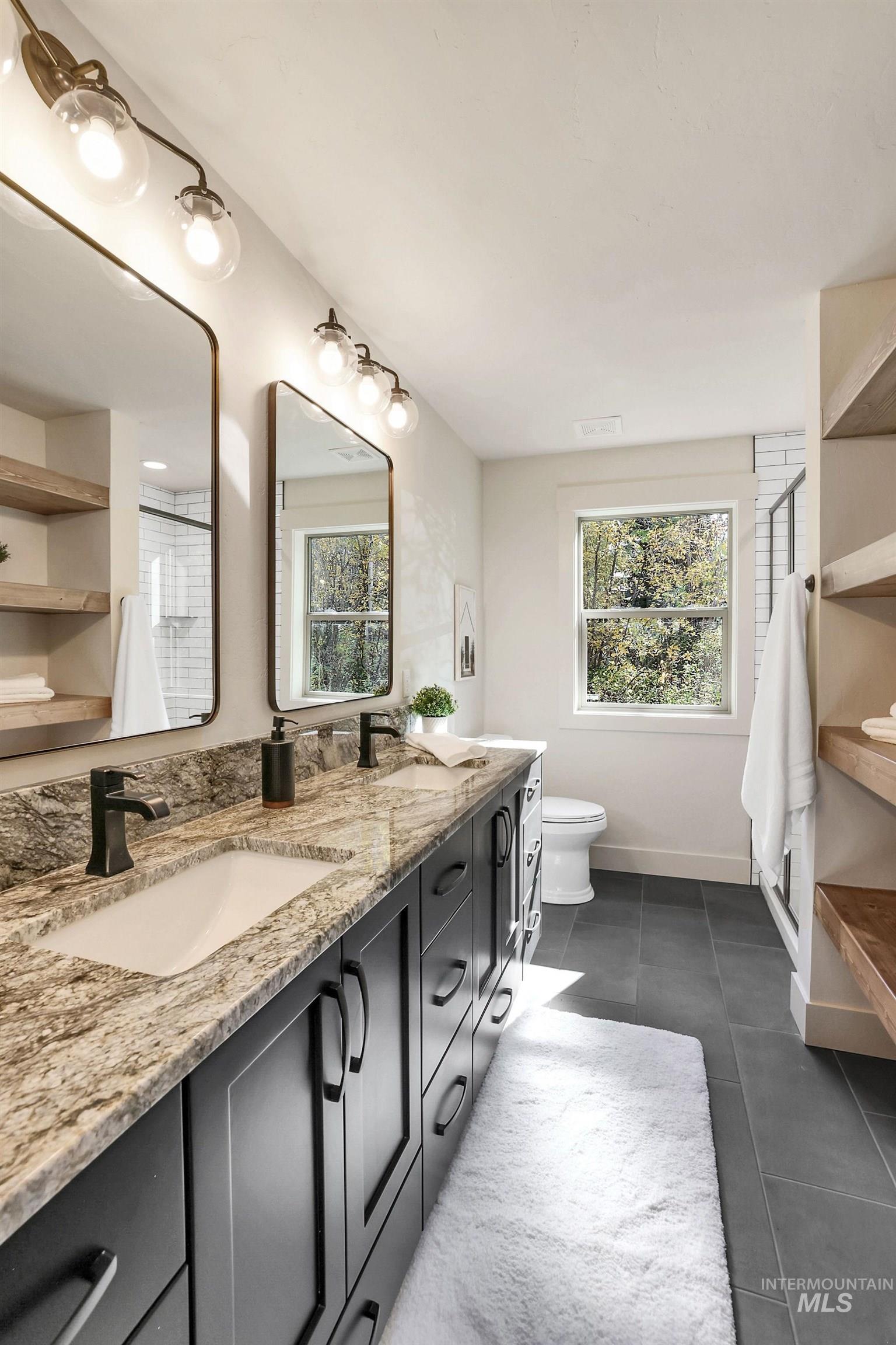 Full bath with double vanity, a stall shower, healthy amount of natural light, and dark tile patterned floors