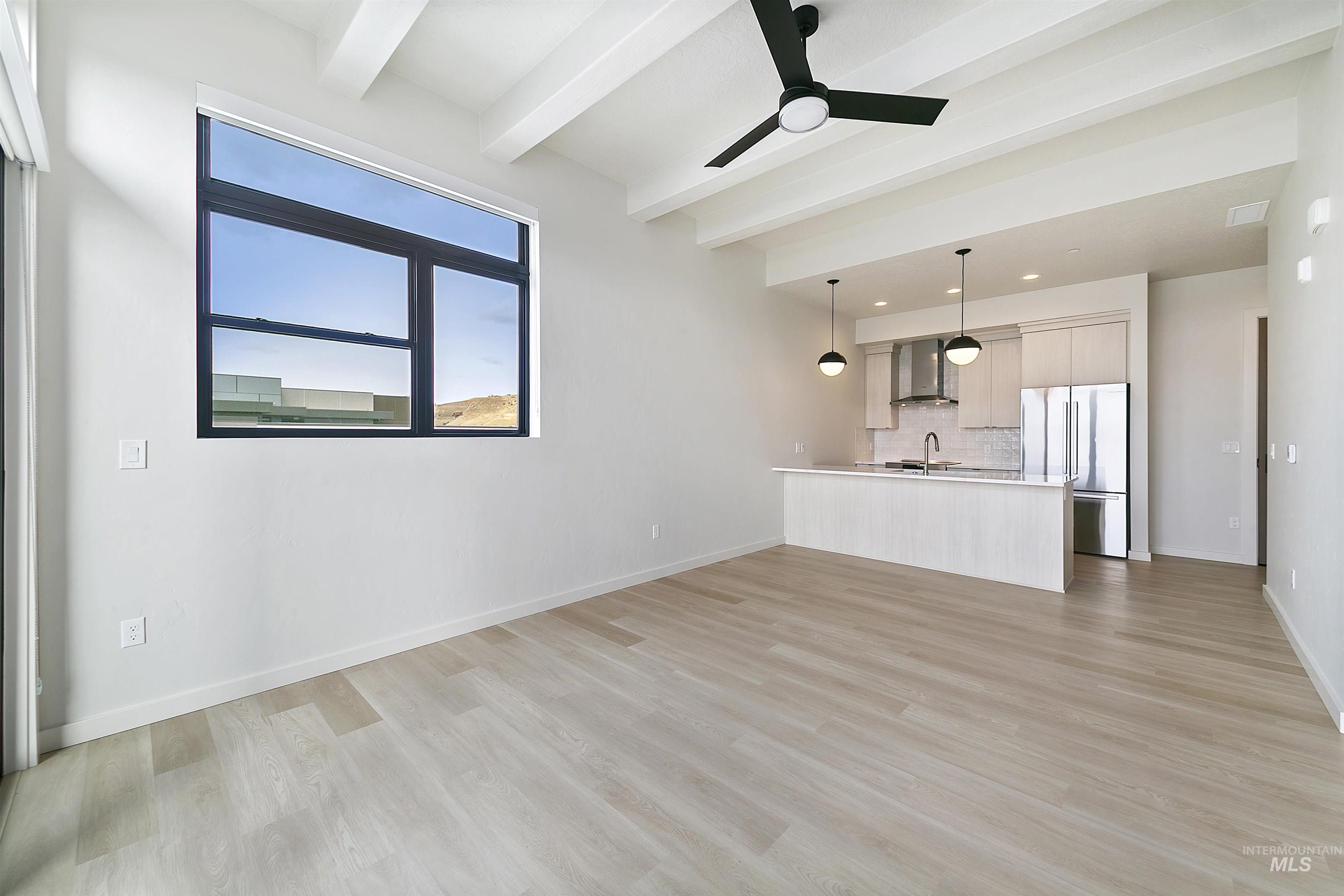 Unfurnished living room featuring a ceiling fan, light wood-style flooring, and beamed ceiling