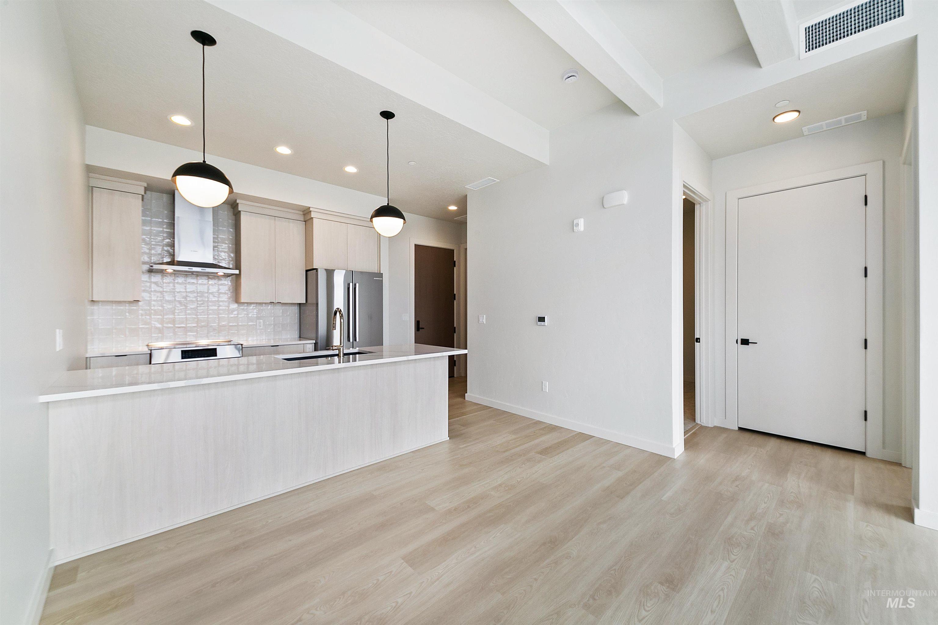 Kitchen featuring hanging light fixtures, stainless steel appliances, tasteful backsplash, wall chimney range hood, and light wood-style floors