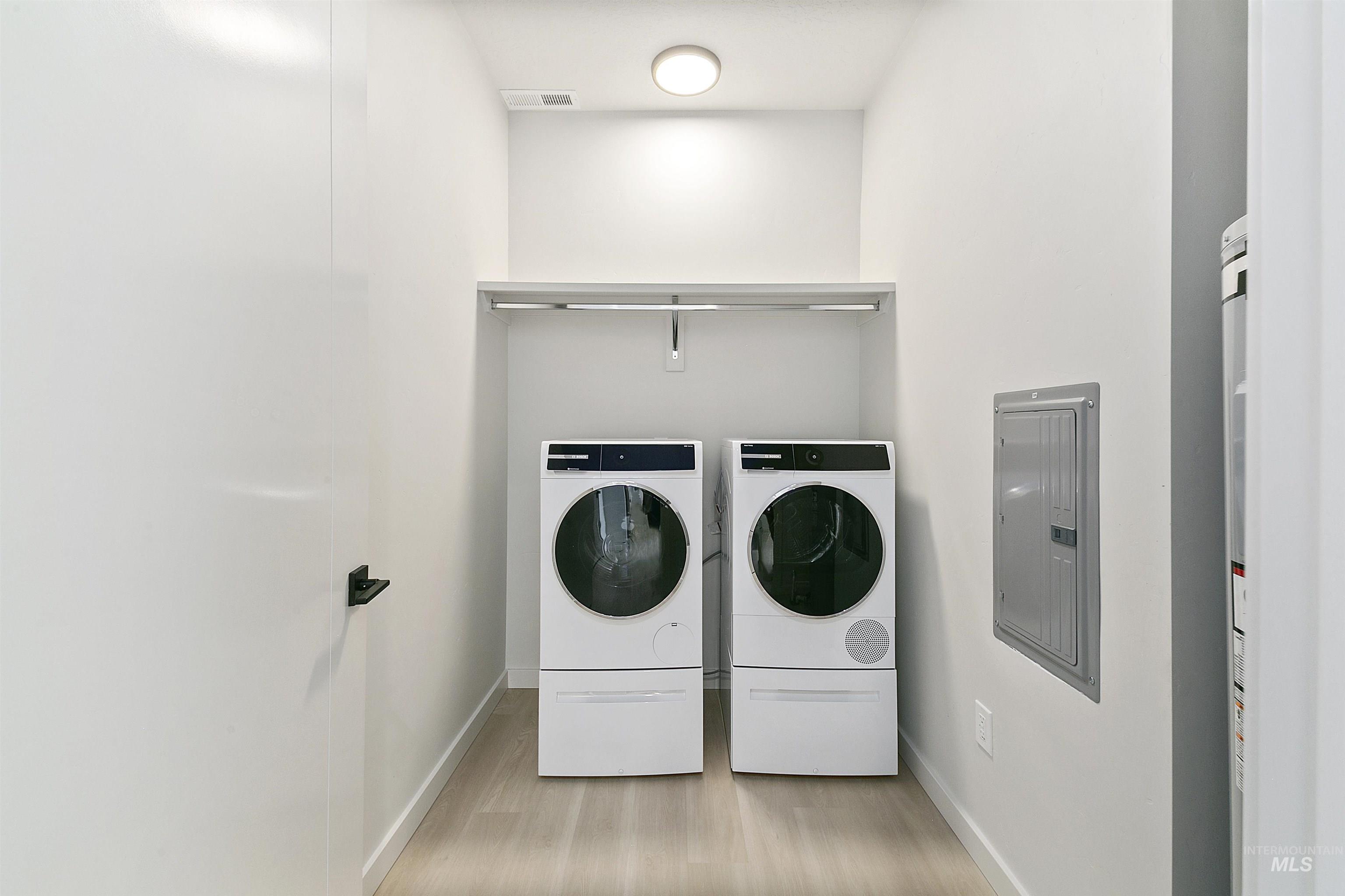 Washroom with electric panel, washing machine and dryer, and light wood-style floors