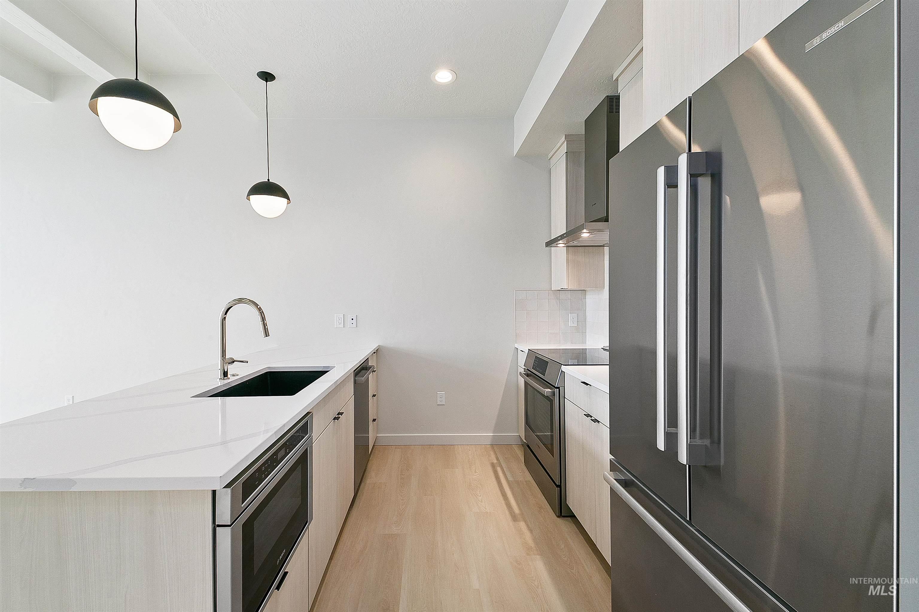 Kitchen featuring appliances with stainless steel finishes, a peninsula, wall chimney exhaust hood, light stone counters, and decorative light fixtures