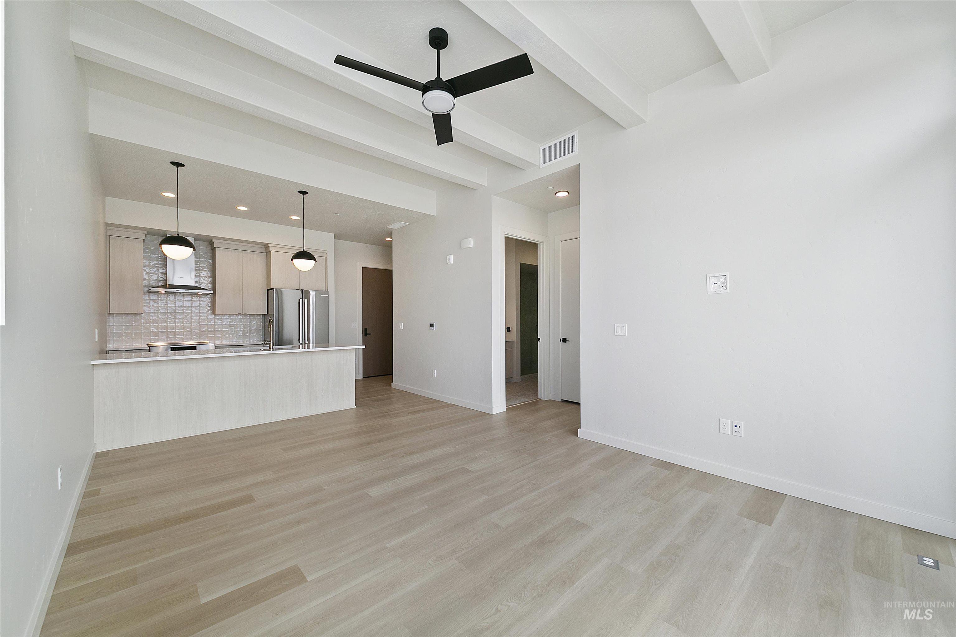 Unfurnished living room with beamed ceiling, ceiling fan, and light wood-type flooring