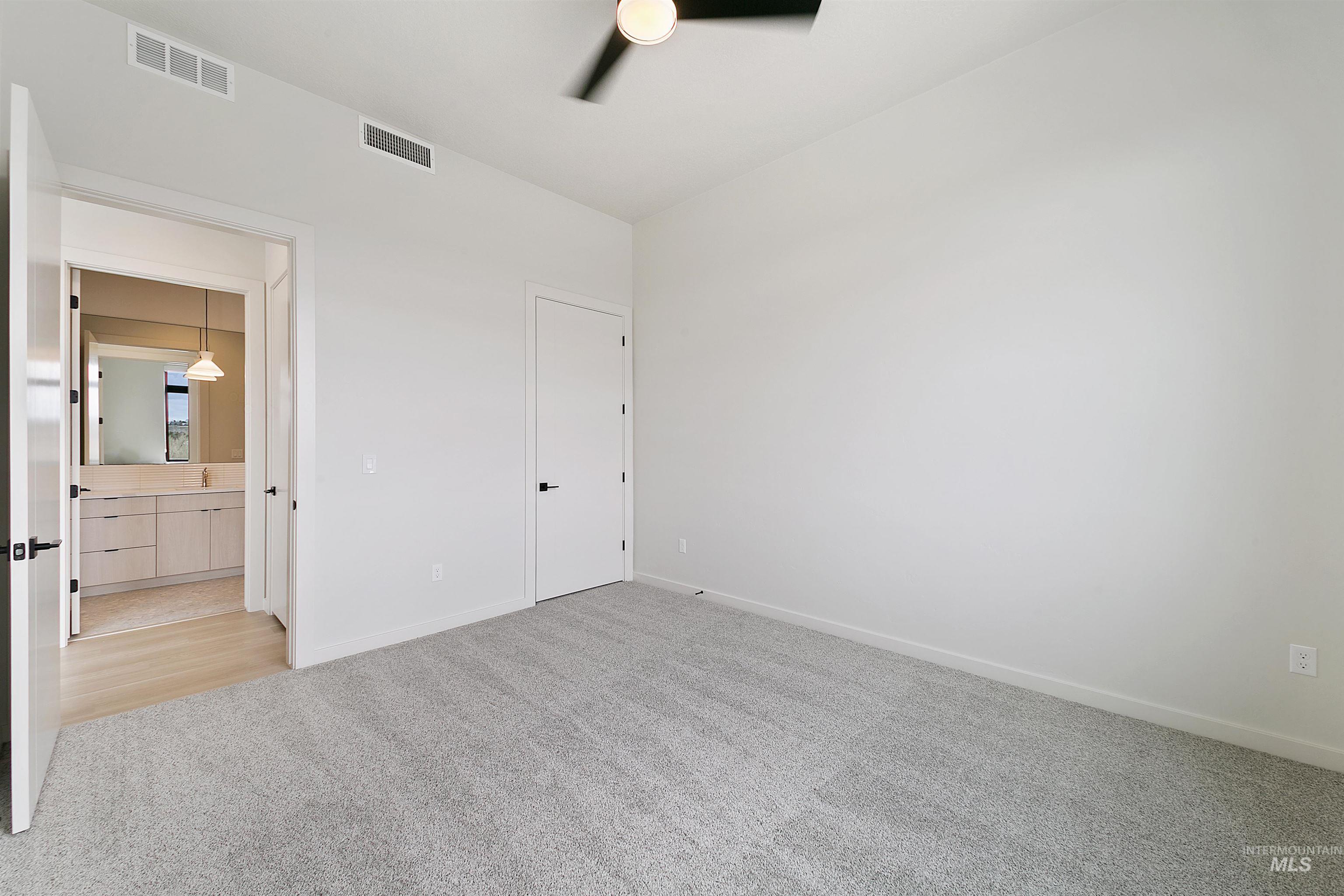 Unfurnished bedroom featuring light carpet, a ceiling fan, and ensuite bath