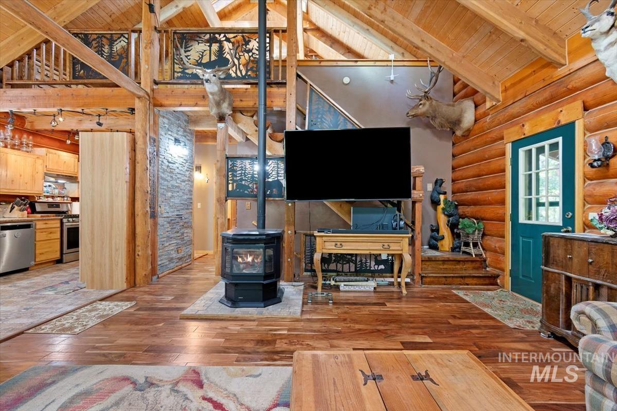 Living area with dark wood-style floors, a high wooden beamed ceiling, a wood stove, and rustic walls