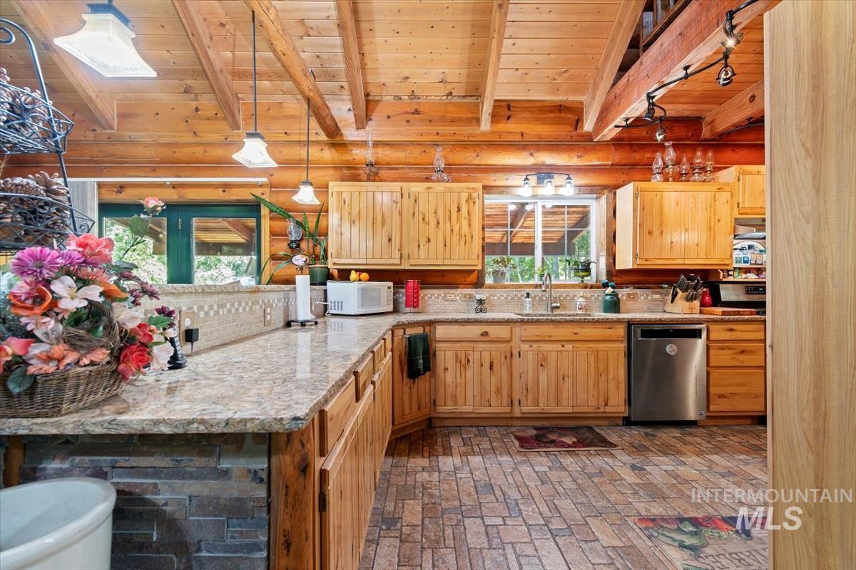 Kitchen with a wooden ceiling with exposed beams, stainless steel dishwasher, white microwave, pendant lighting, and a peninsula