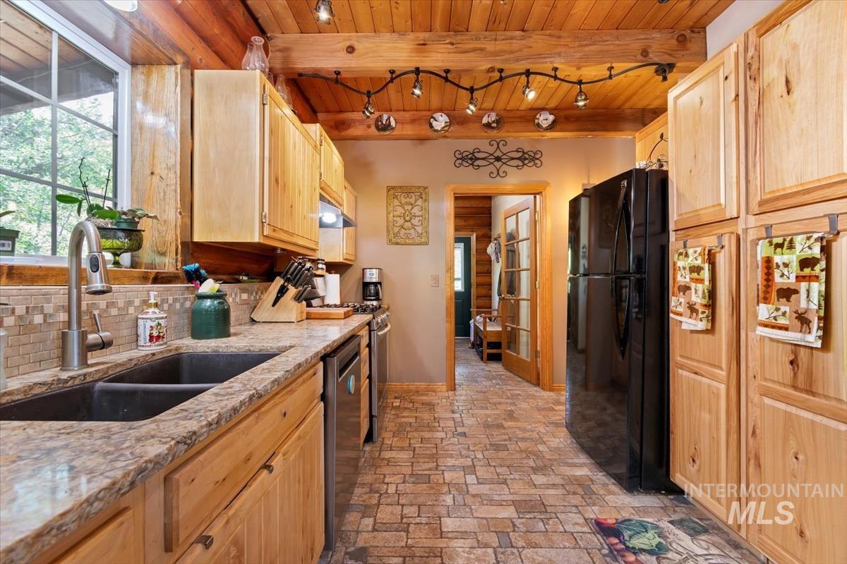 Kitchen with light wood finish cabinets, stainless steel appliances, a wood ceiling with exposed beams, light stone counters, and track lighting