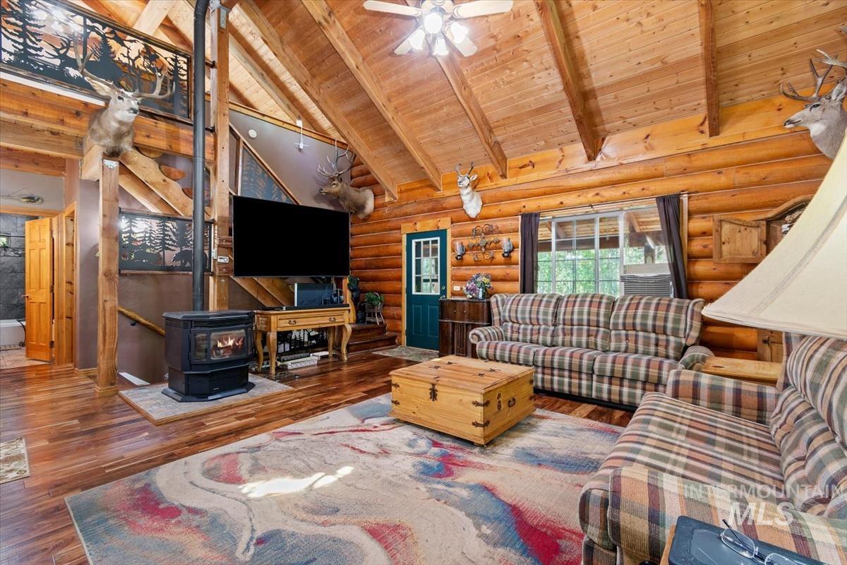 Living area with a wood stove, a high wood beamed ceiling, wood-type flooring, log walls, and a ceiling fan