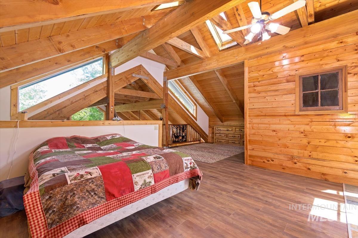 Bedroom featuring a skylight, wood walls, a wooden ceiling with exposed beams, wood finished floors, and a ceiling fan