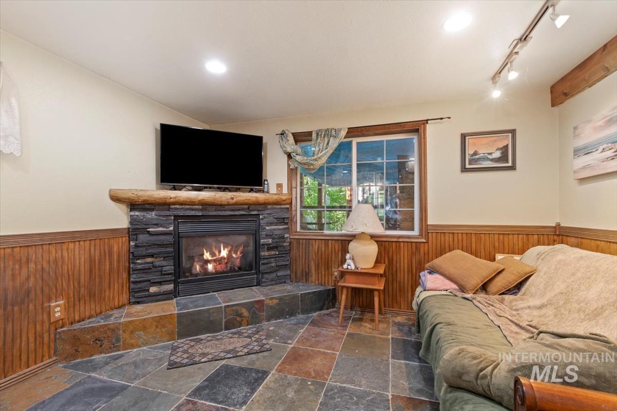 Living room featuring wooden walls, wainscoting, stone tile floors, a tiled fireplace, and track lighting