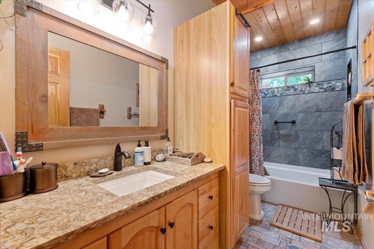 Full bath featuring vanity, shower / bath combo with shower curtain, light stone finish floors, and recessed lighting
