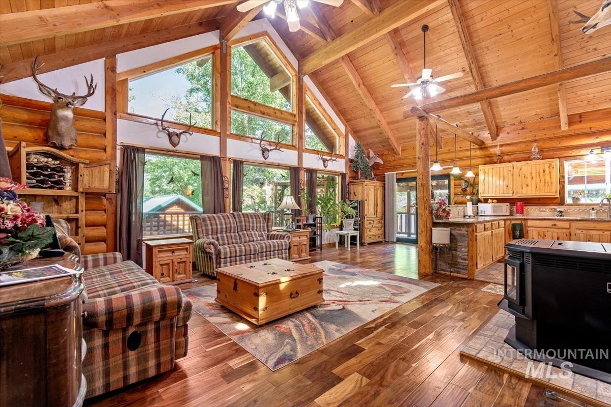 Living room featuring a high wood beamed ceiling, dark wood-type flooring, a wood stove, and ceiling fan