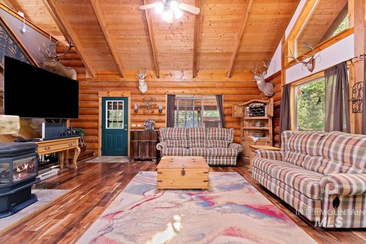 Living room featuring a high wood beamed ceiling, dark wood finished floors, a wood stove, a ceiling fan, and rustic walls