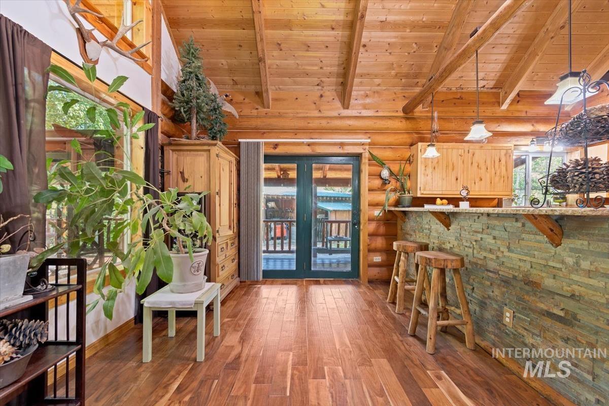 Interior space with a high wooden beamed ceiling, dark wood-type flooring, french doors, log walls, and pendant lighting