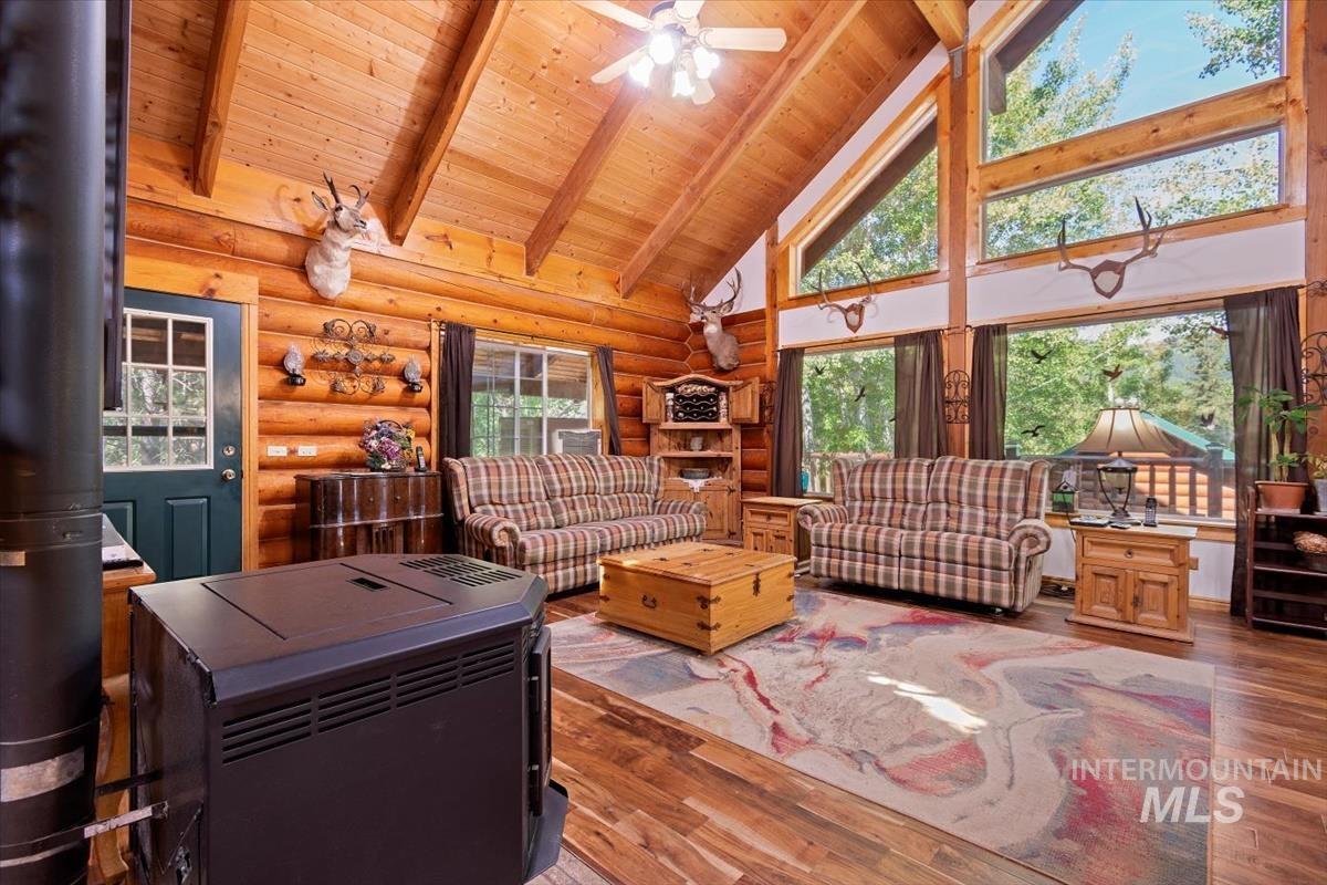 Living area featuring rustic walls, a high wooden beamed ceiling, wood-type flooring, and ceiling fan