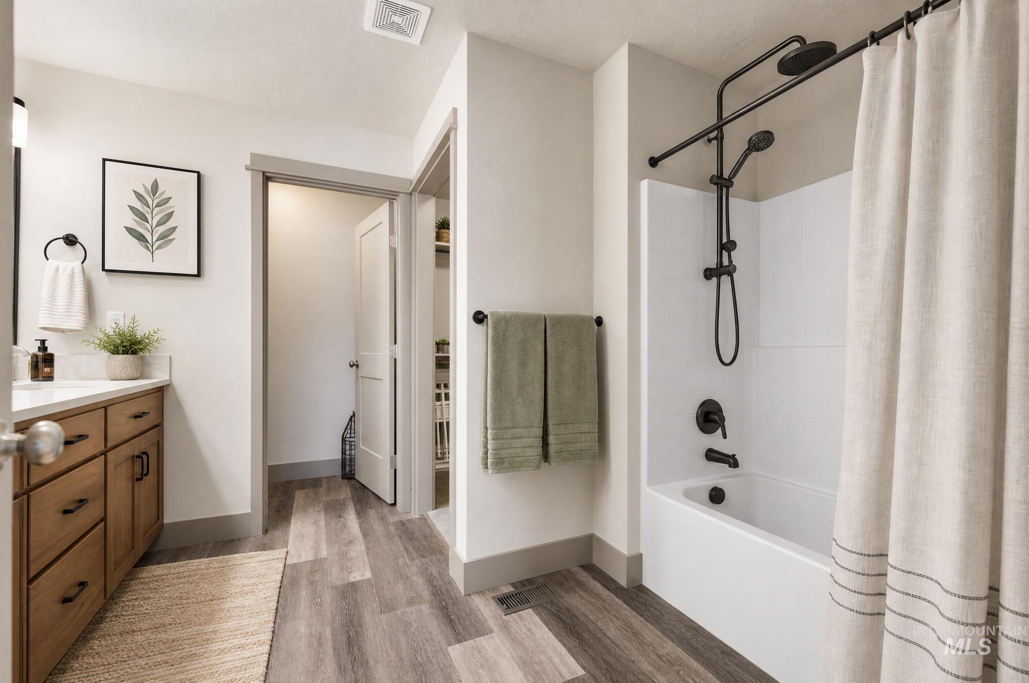 Bathroom featuring a white tub with matte black fixtures, a wood-finish vanity with a white countertop, and gray wood-finish flooring