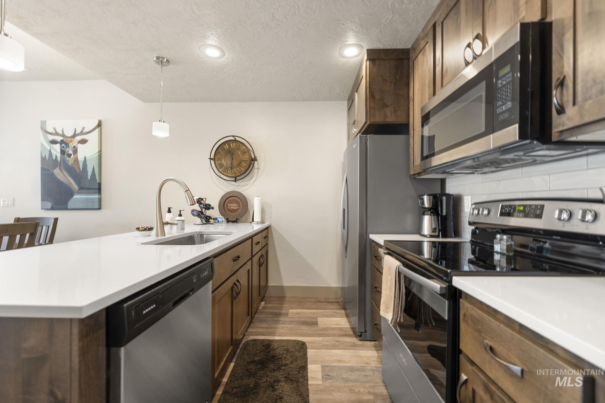 Kitchen featuring stainless steel appliances, wood-finish flooring, recessed lighting, and a white countertop island with an undermount sink