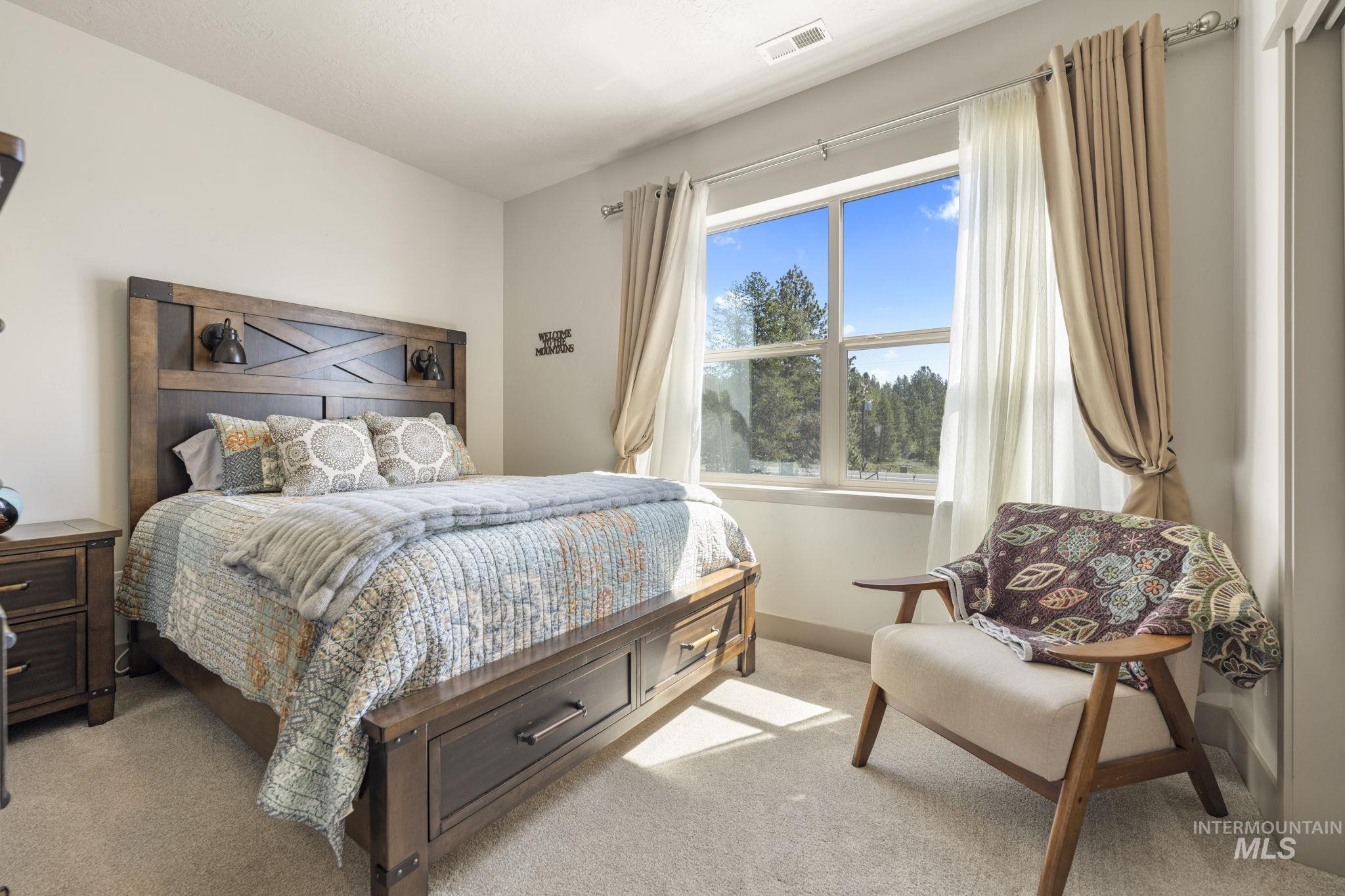 Window-equipped bedroom featuring light-colored carpeting, a dark wood-finish bed frame with built-in storage drawers, and wall-mounted sconces on the headboard