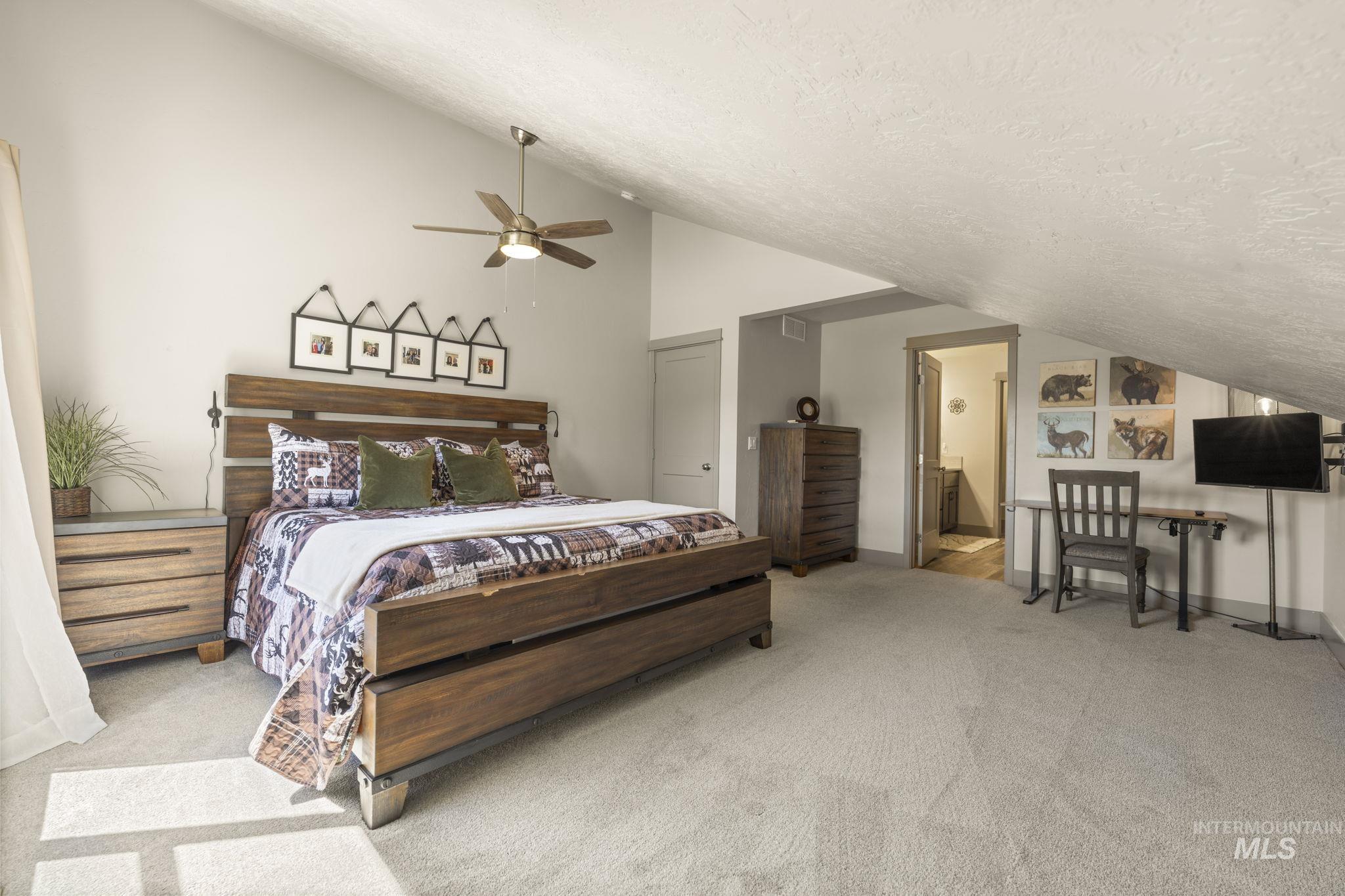 Spacious bedroom featuring light neutral wall tones, vaulted ceiling, and carpeted flooring