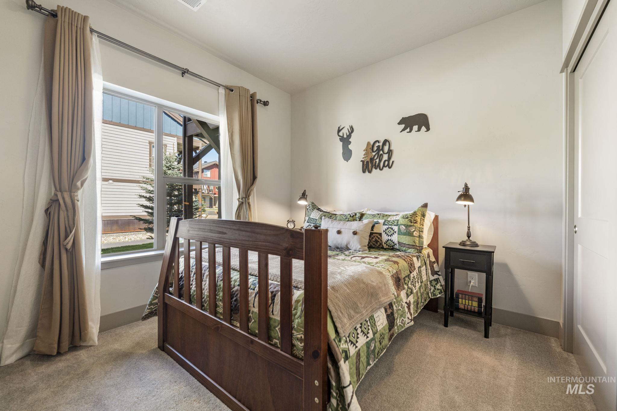 Carpeted room featuring a large window with white trim, soft beige window treatments, light-colored walls, and a sliding closet door