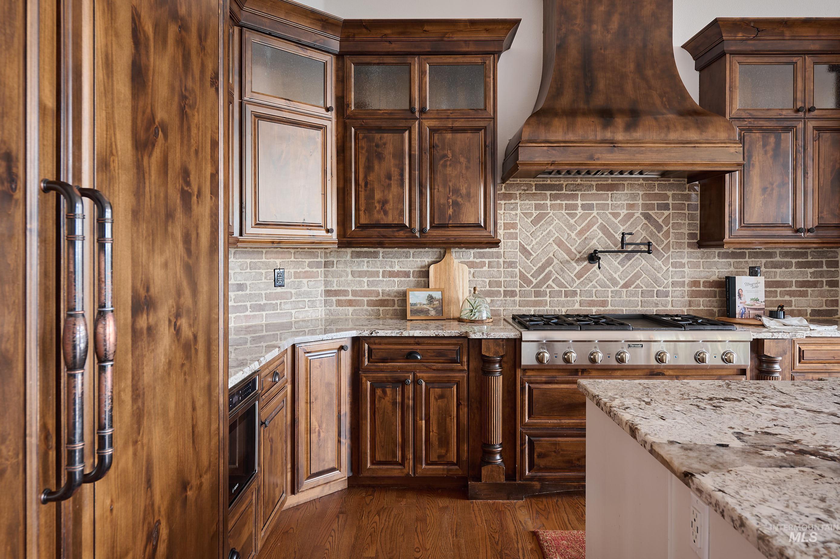 Kitchen with light stone counters, backsplash, custom exhaust hood, dark wood finished floors, and stainless steel gas cooktop