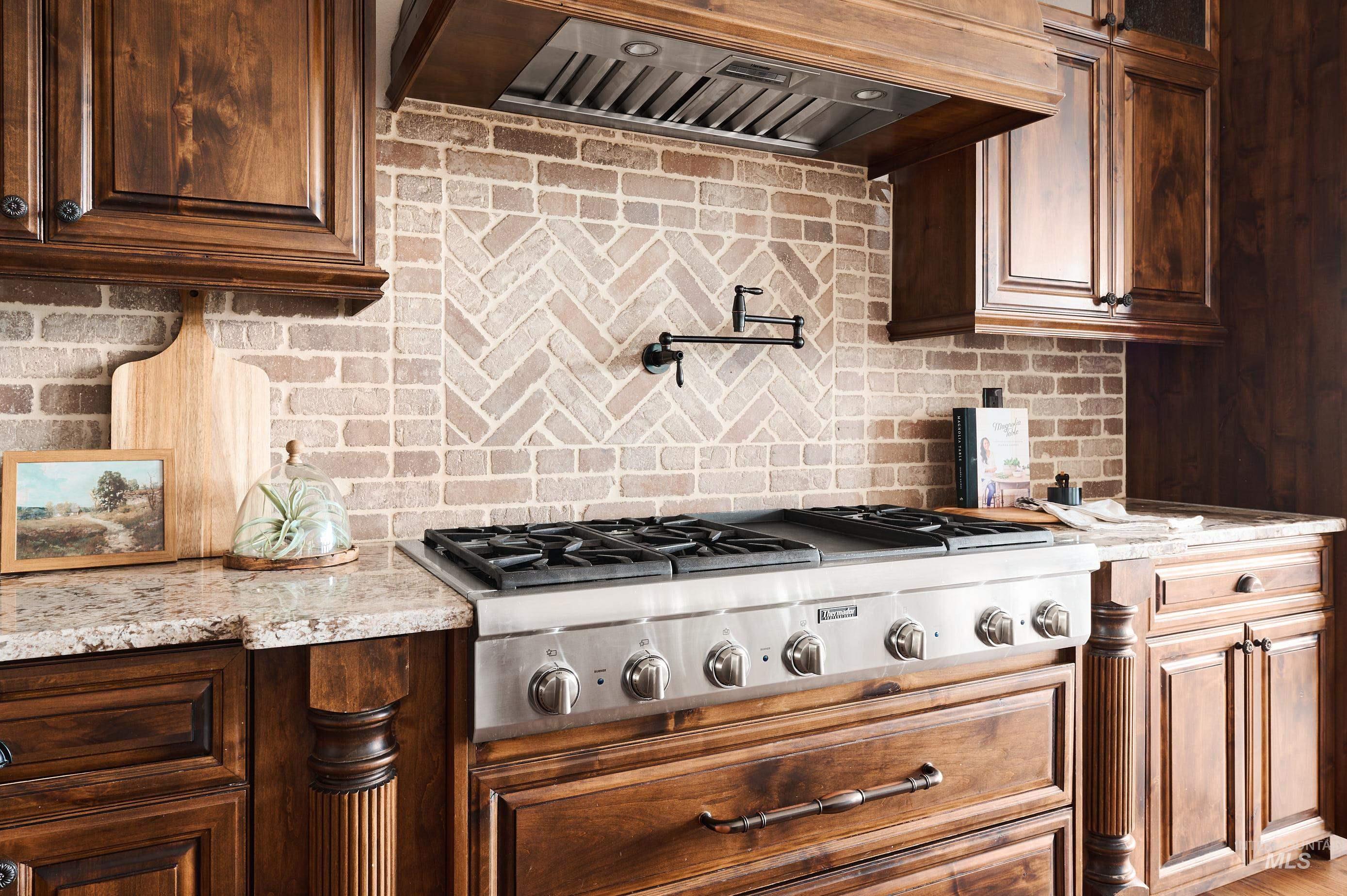 Kitchen featuring custom exhaust hood, tasteful backsplash, stainless steel gas cooktop, and light stone countertops