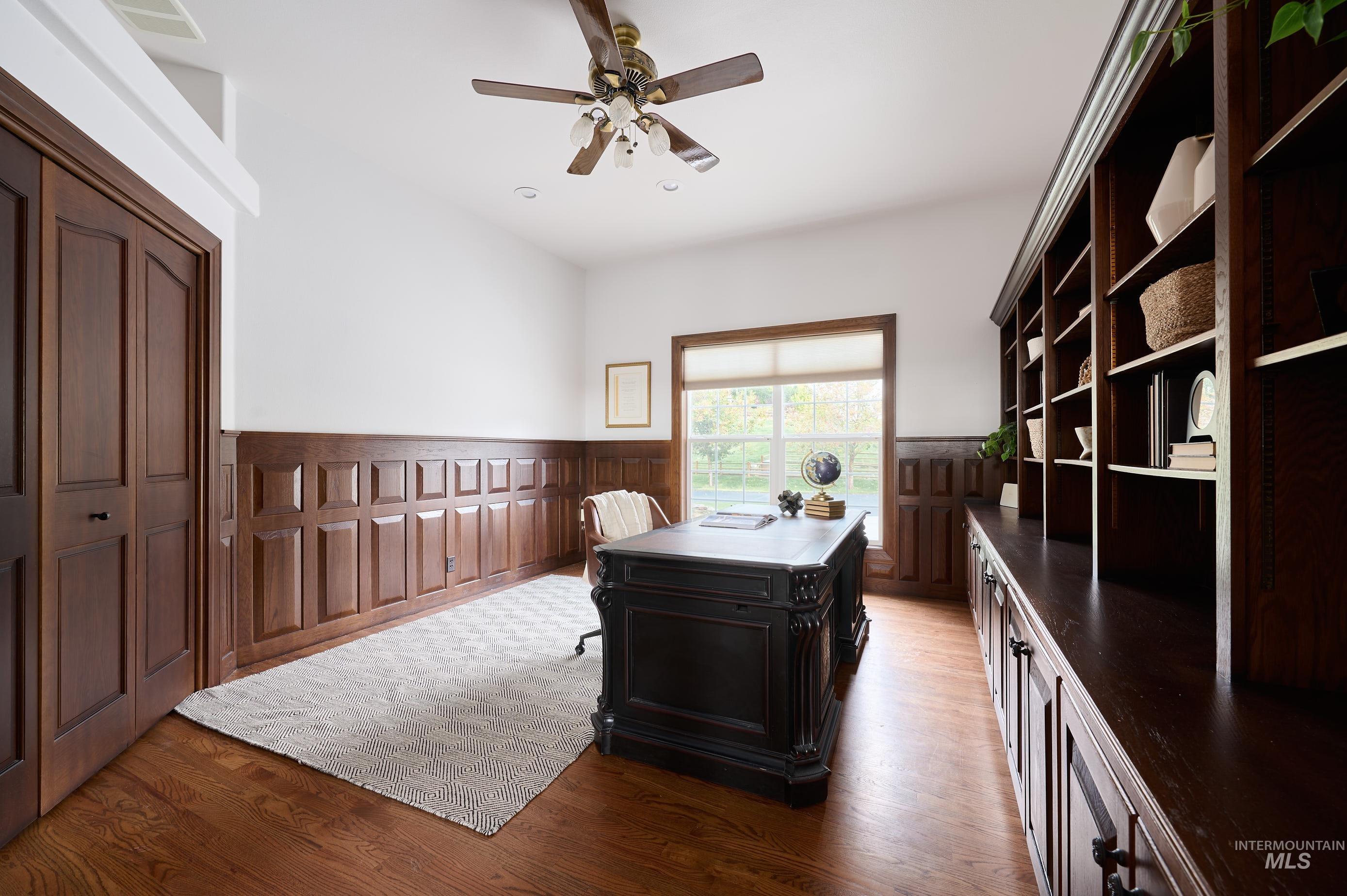 Office area with dark wood finished floors, wainscoting, and a ceiling fan