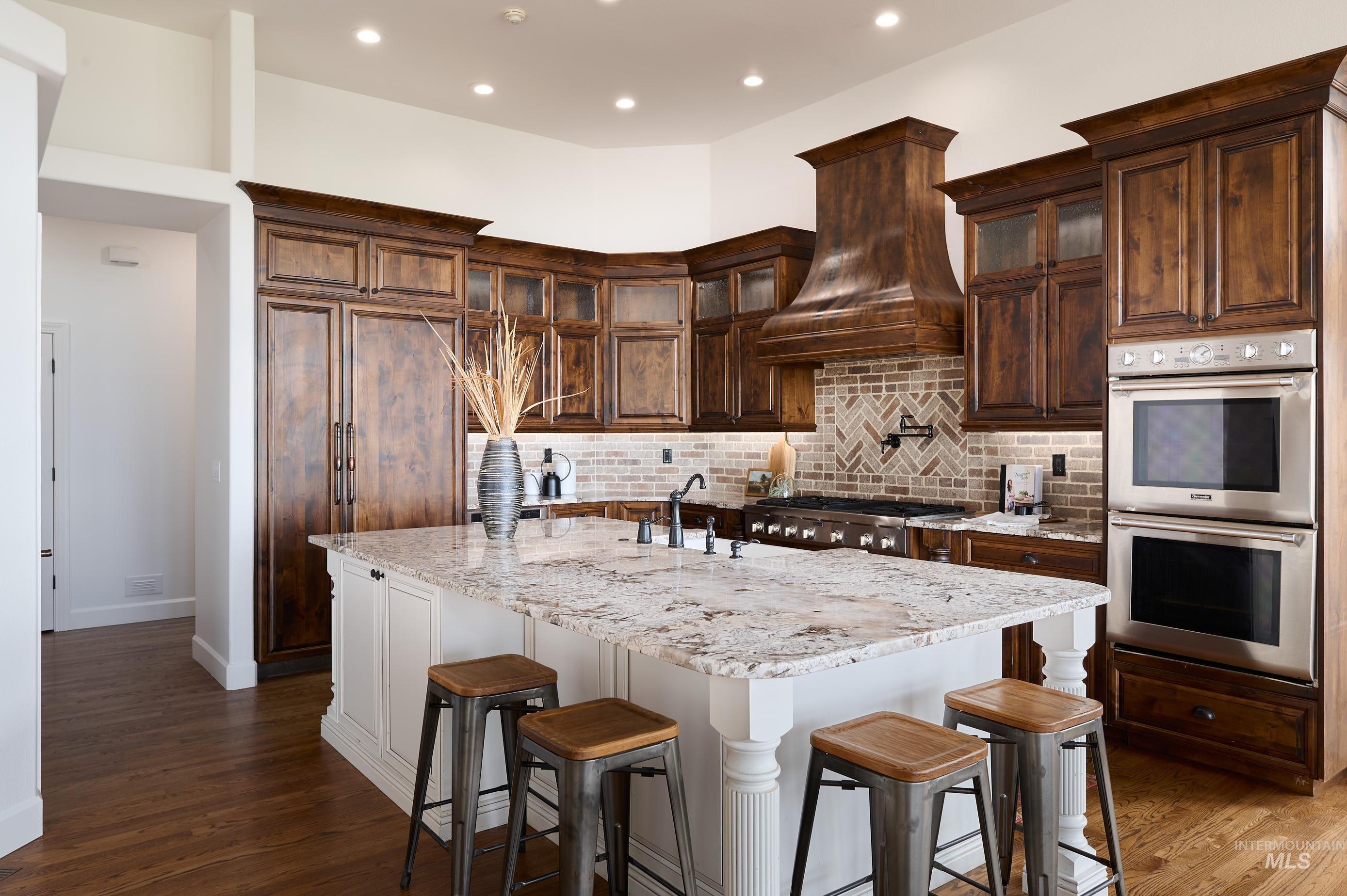 Kitchen featuring a breakfast bar, decorative backsplash, appliances with stainless steel finishes, glass insert cabinets, and light stone countertops
