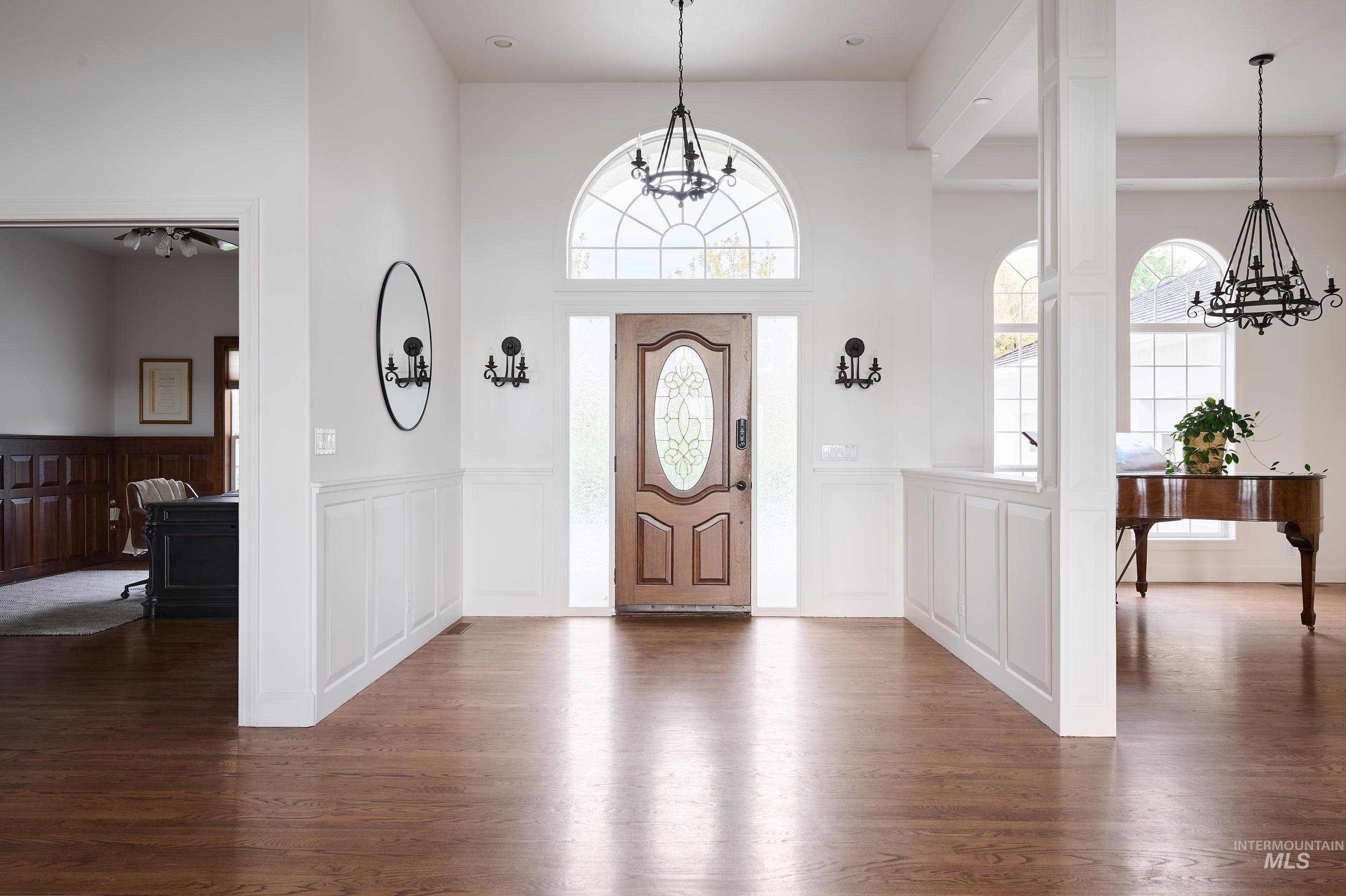 Entryway with a chandelier, dark wood-type flooring, a wainscoted wall, a decorative wall, and a towering ceiling