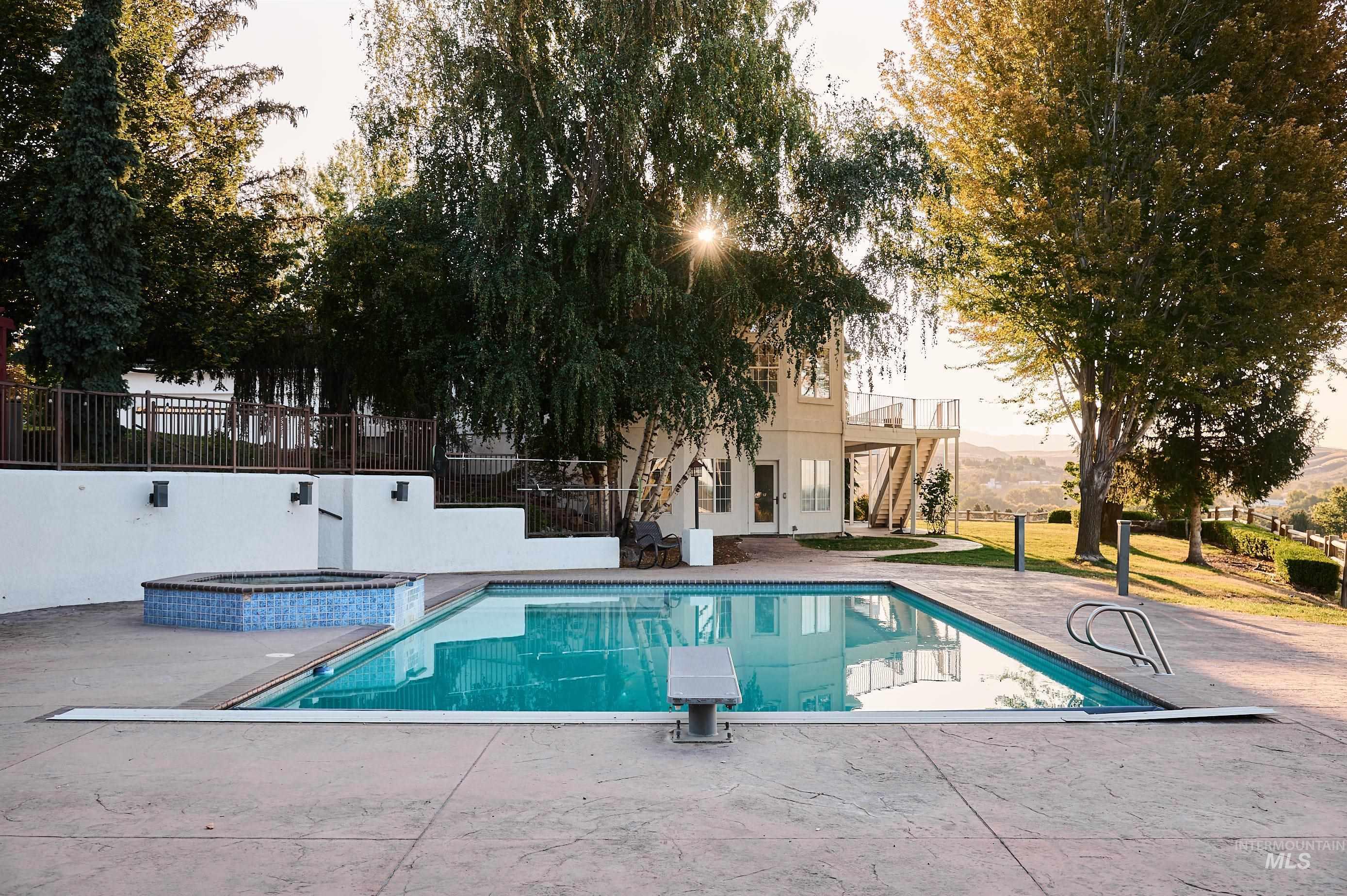 View of pool featuring a patio area, stairway, a diving board, a pool with connected hot tub, and a balcony