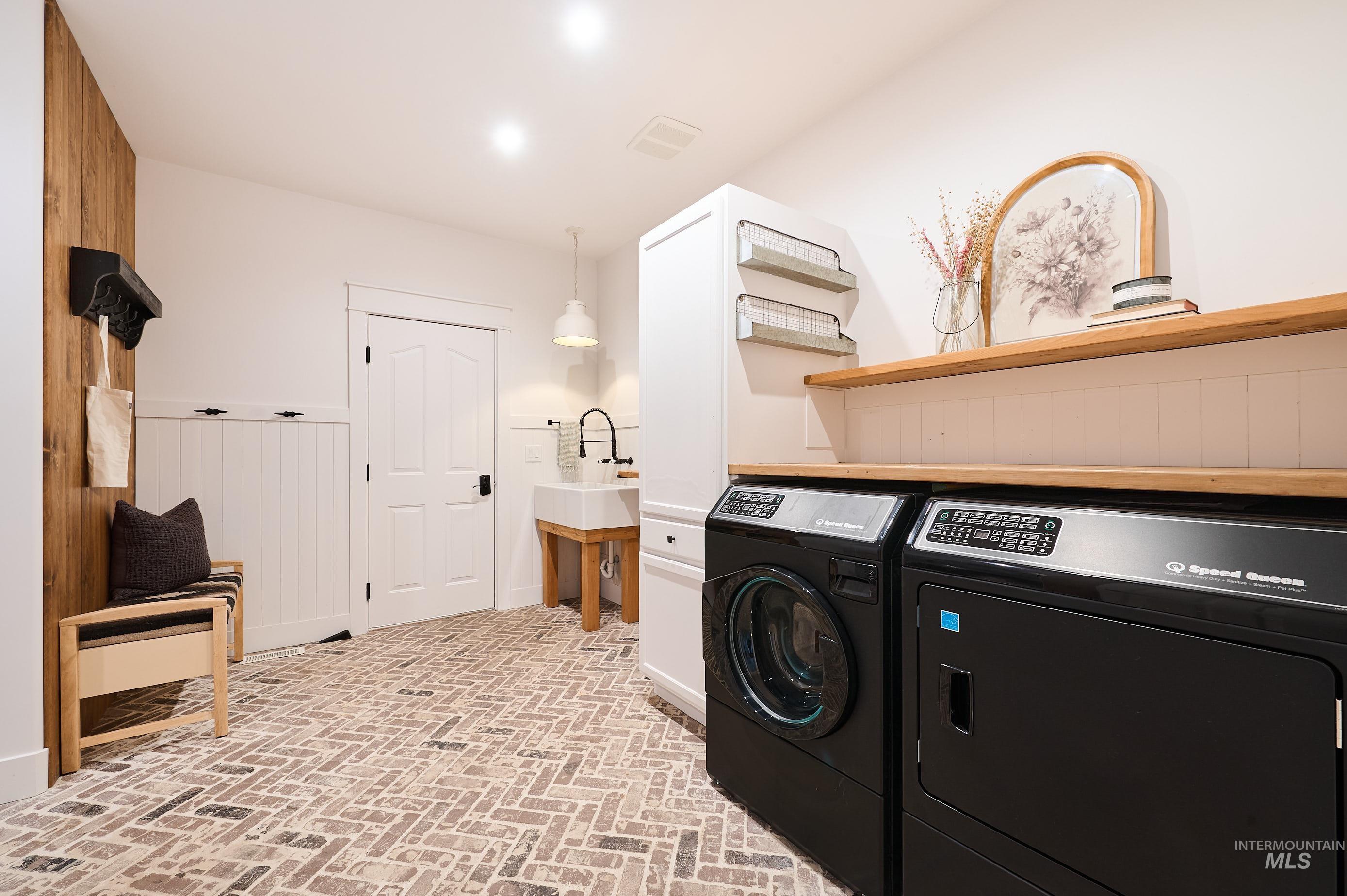 Washroom with brick flooring, separate washer and dryer, and wood walls