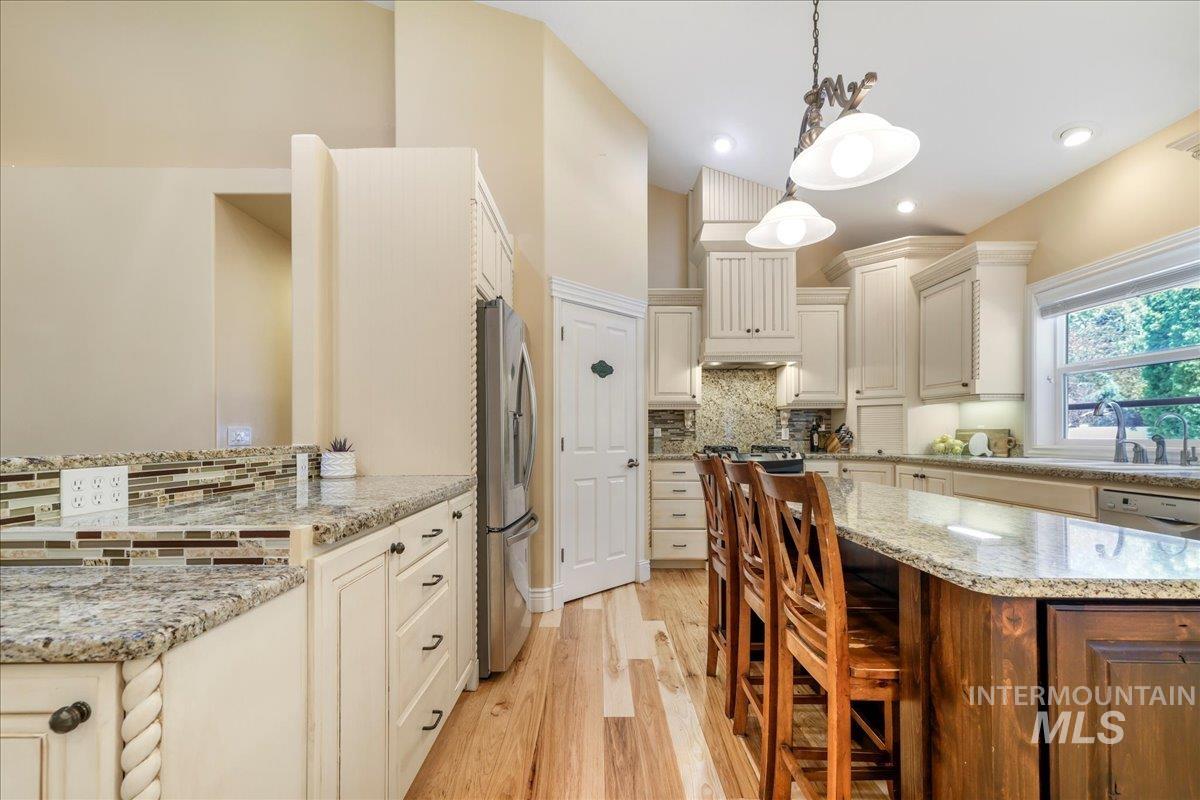 Kitchen featuring freestanding refrigerator, tasteful backsplash, light wood finished floors, a kitchen bar, and pendant lighting