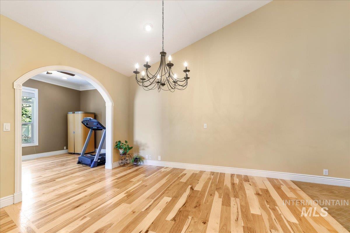 Empty room featuring arched walkways, a chandelier, light wood-type flooring, and high vaulted ceiling