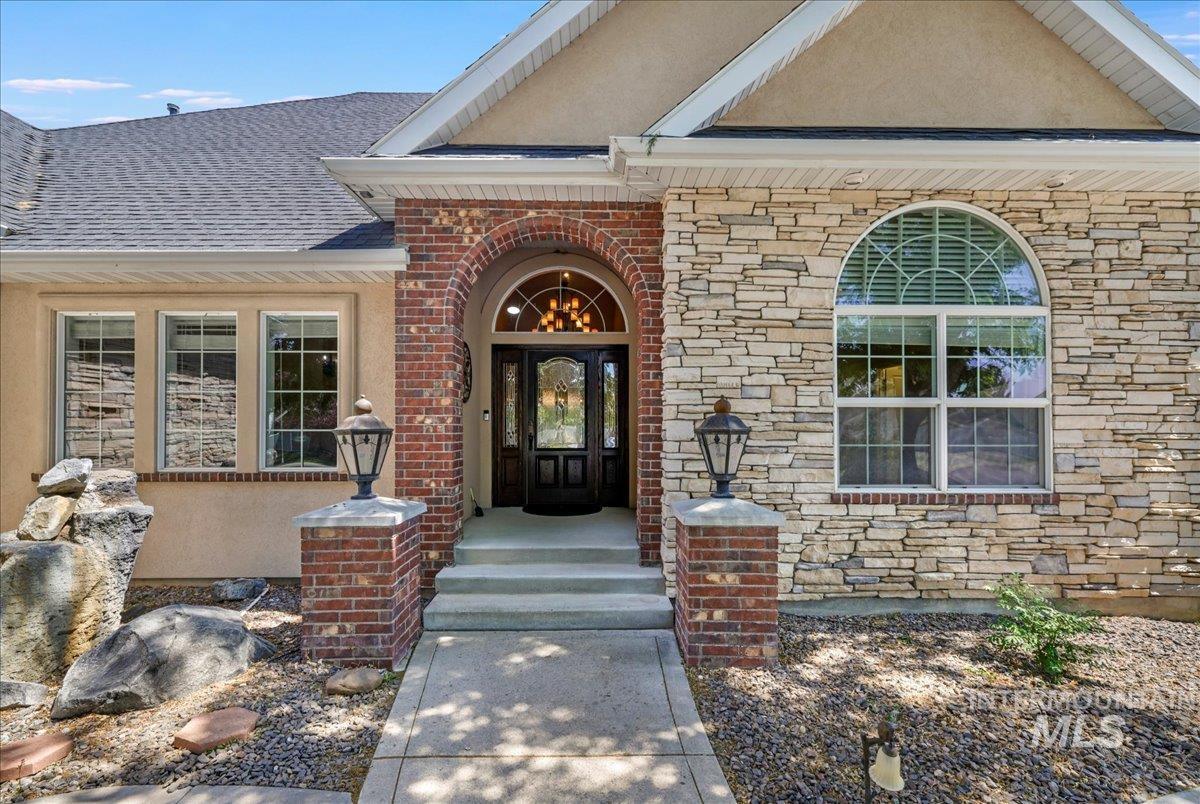 Doorway to property with stucco siding, stone siding, roof with shingles, and brick siding