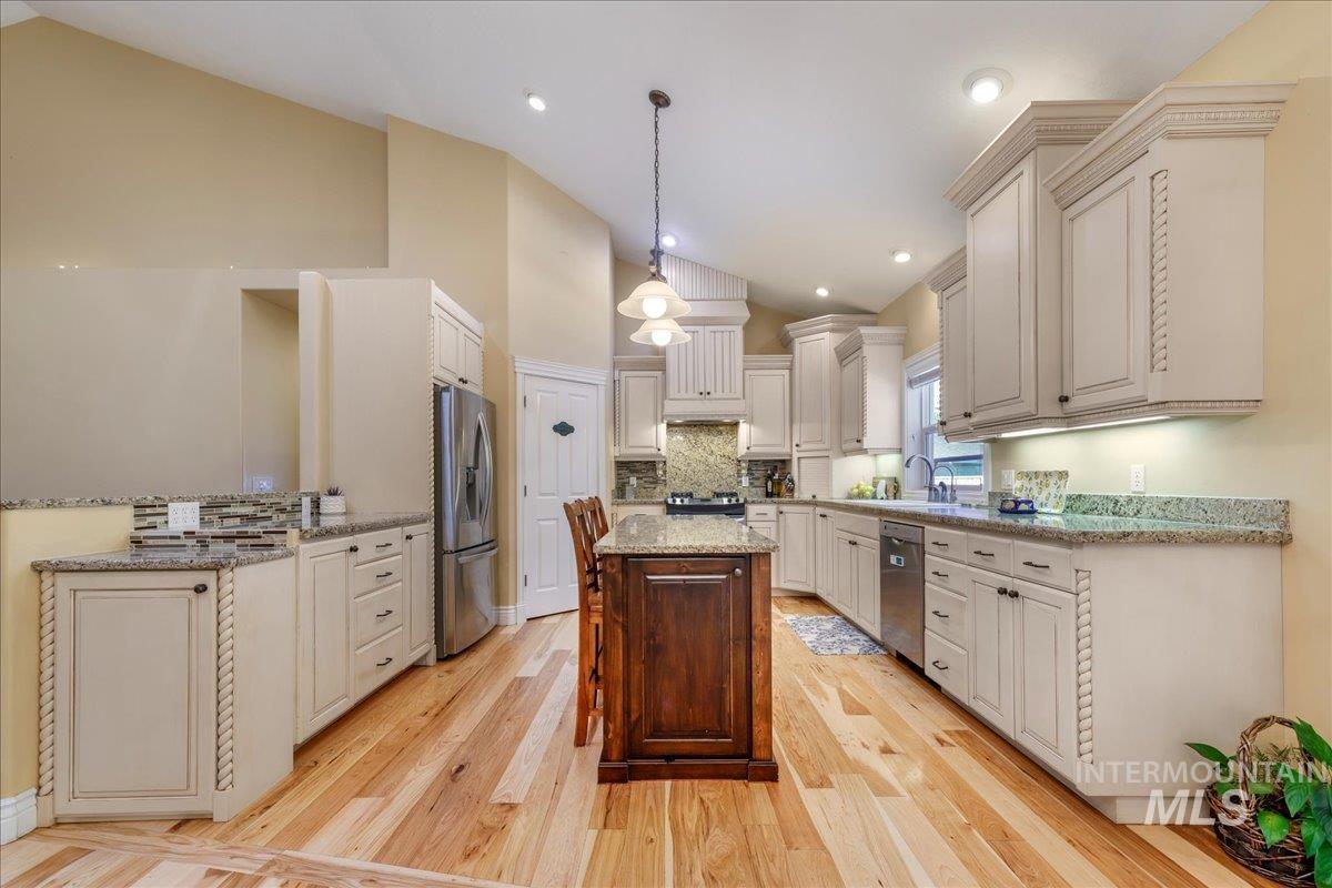 Kitchen with appliances with stainless steel finishes, a kitchen island, backsplash, light wood-style flooring, and high vaulted ceiling