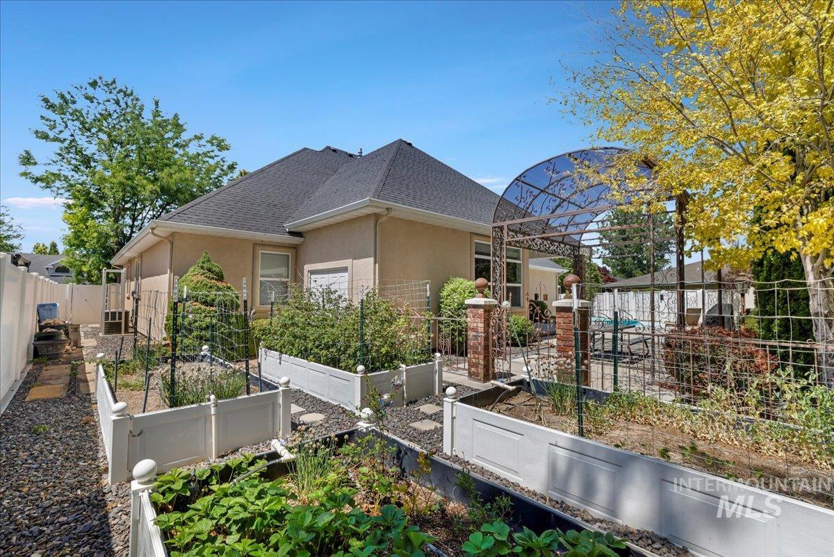 View of side of property with a garden, stucco siding, roof with shingles, and a fenced backyard