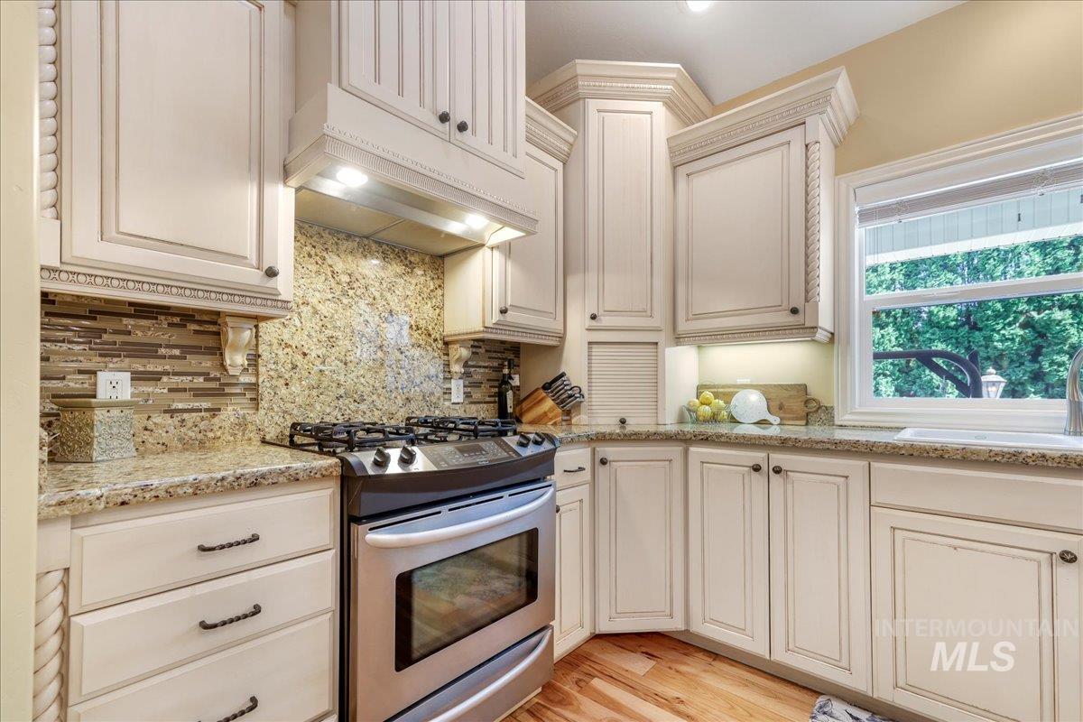 Kitchen featuring stainless steel gas stove, backsplash, light wood-style flooring, light stone countertops, and premium range hood