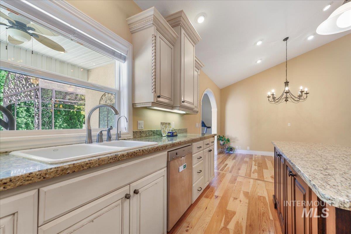 Kitchen with stainless steel dishwasher, light wood-style flooring, lofted ceiling, arched walkways, and pendant lighting