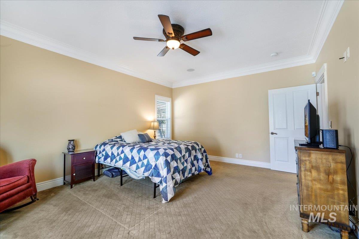 Bedroom with light colored carpet, ornamental molding, and ceiling fan