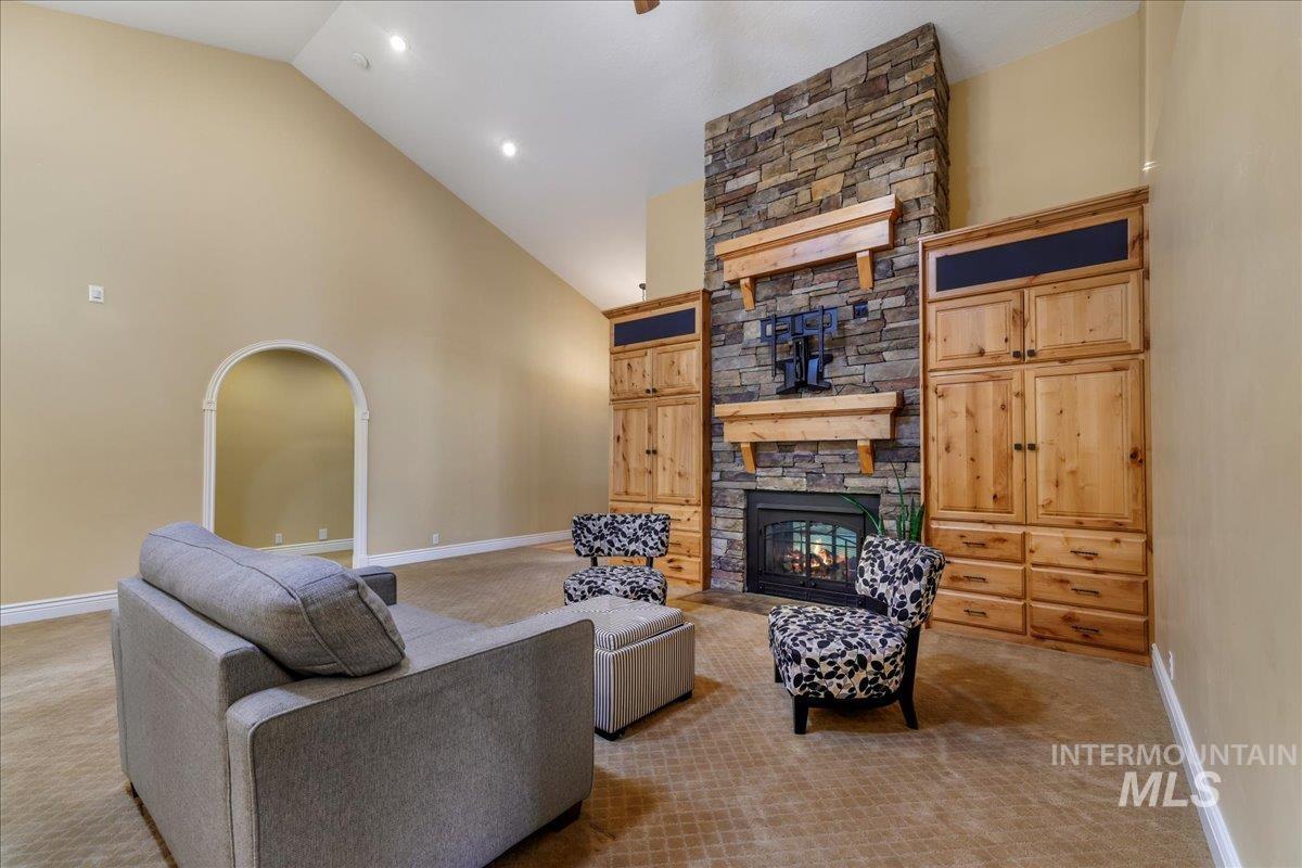 Living room with a stone fireplace, carpet floors, high vaulted ceiling, and recessed lighting