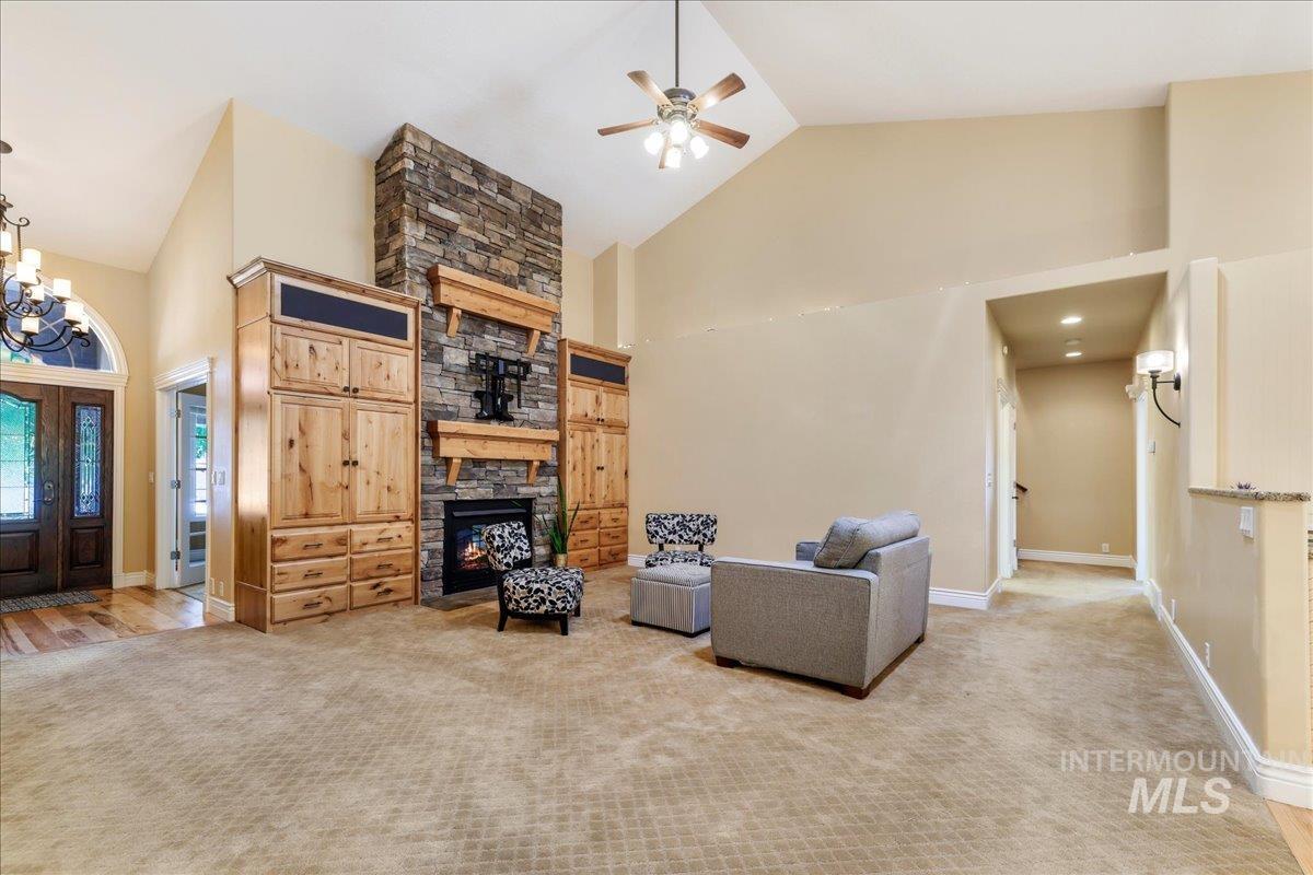 Living room featuring high vaulted ceiling, a fireplace, ceiling fan, carpet, and a chandelier