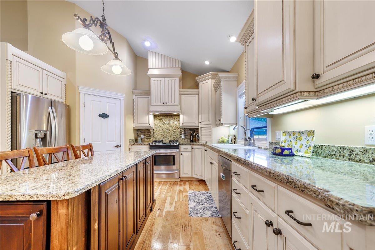 Kitchen featuring appliances with stainless steel finishes, backsplash, light wood-style floors, light stone counters, and decorative light fixtures
