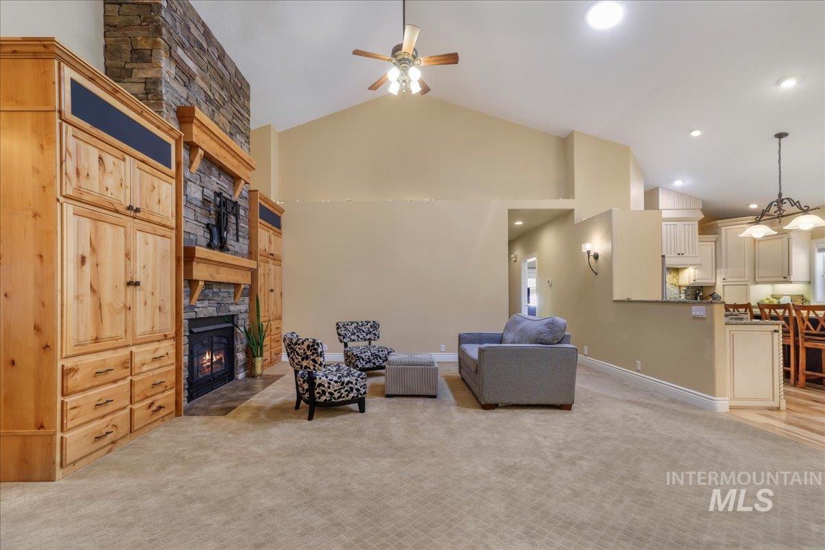 Living area featuring a stone fireplace, light colored carpet, ceiling fan, high vaulted ceiling, and recessed lighting