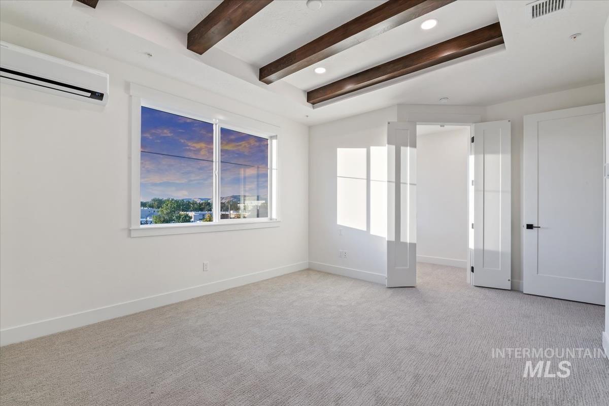Unfurnished room featuring light carpet, a wall mounted air conditioner, and beam ceiling