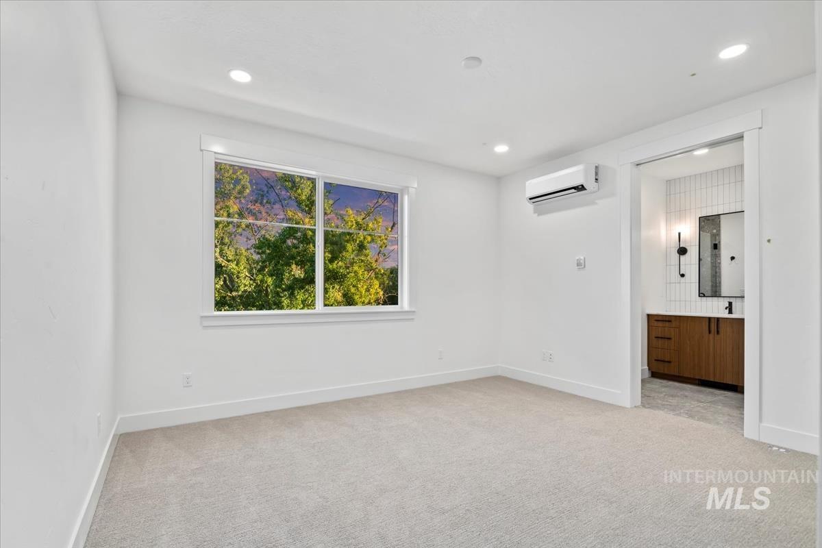 Unfurnished bedroom featuring light carpet, recessed lighting, ensuite bath, and an AC wall unit