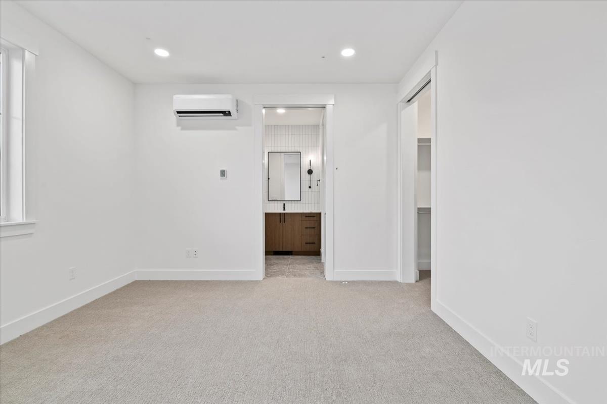 Unfurnished bedroom featuring light colored carpet, recessed lighting, a wall mounted air conditioner, and ensuite bathroom