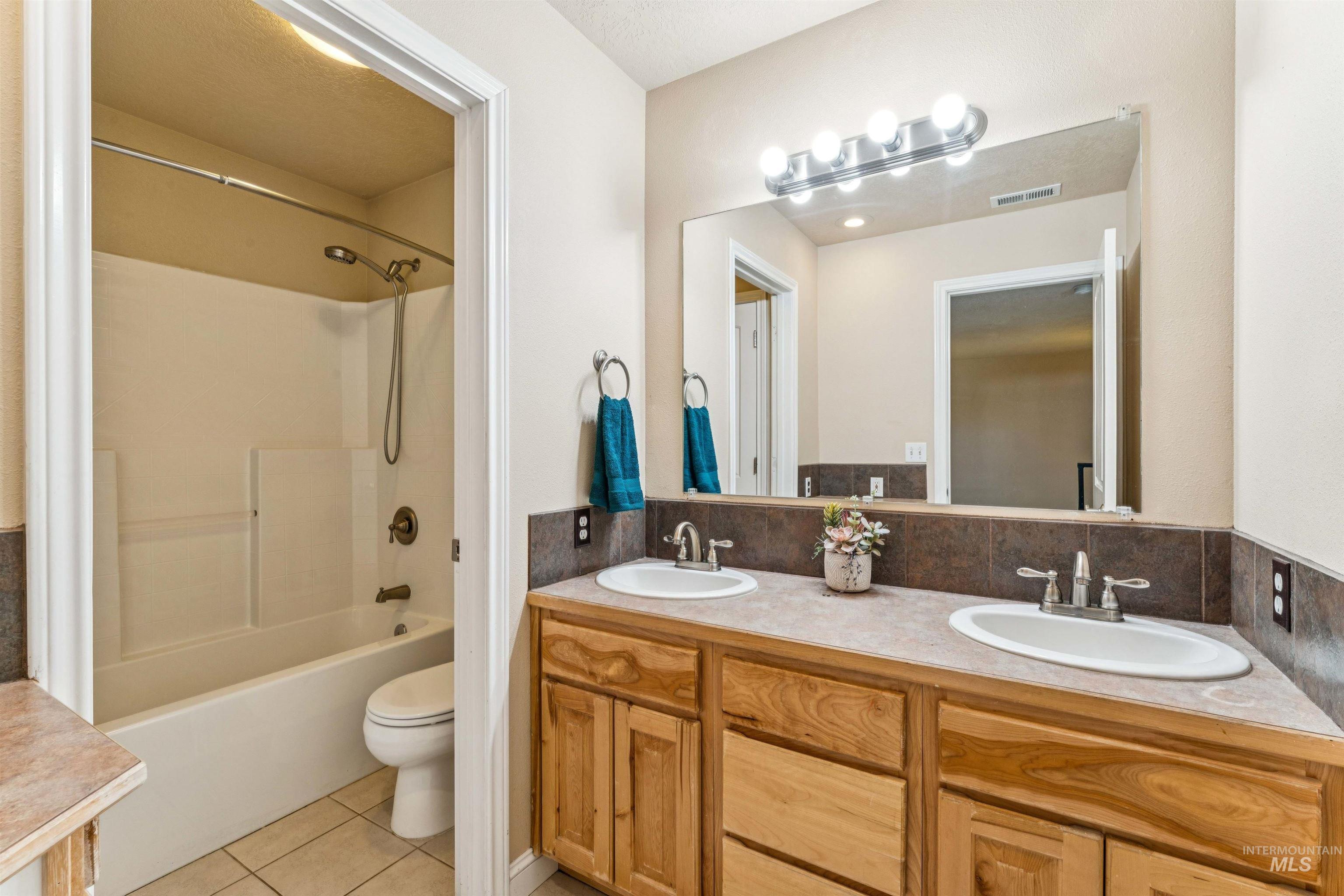 Full bath with light tile patterned flooring, bathtub / shower combination, double vanity, and tasteful backsplash